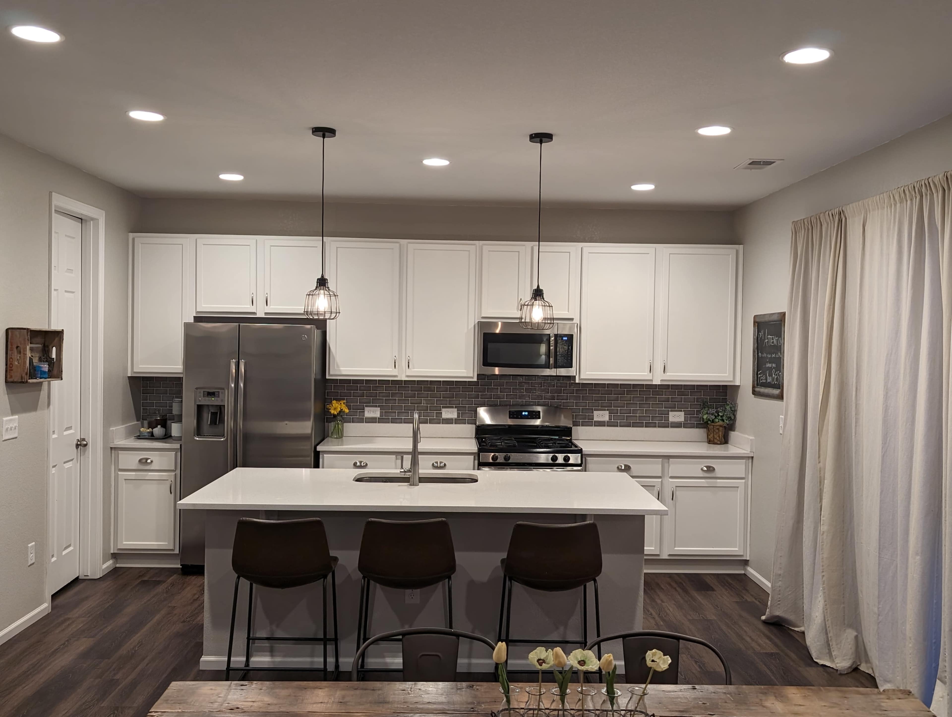 A modern kitchen with white cabinetry, stainless steel appliances, a central island with seating, and a gray backsplash.