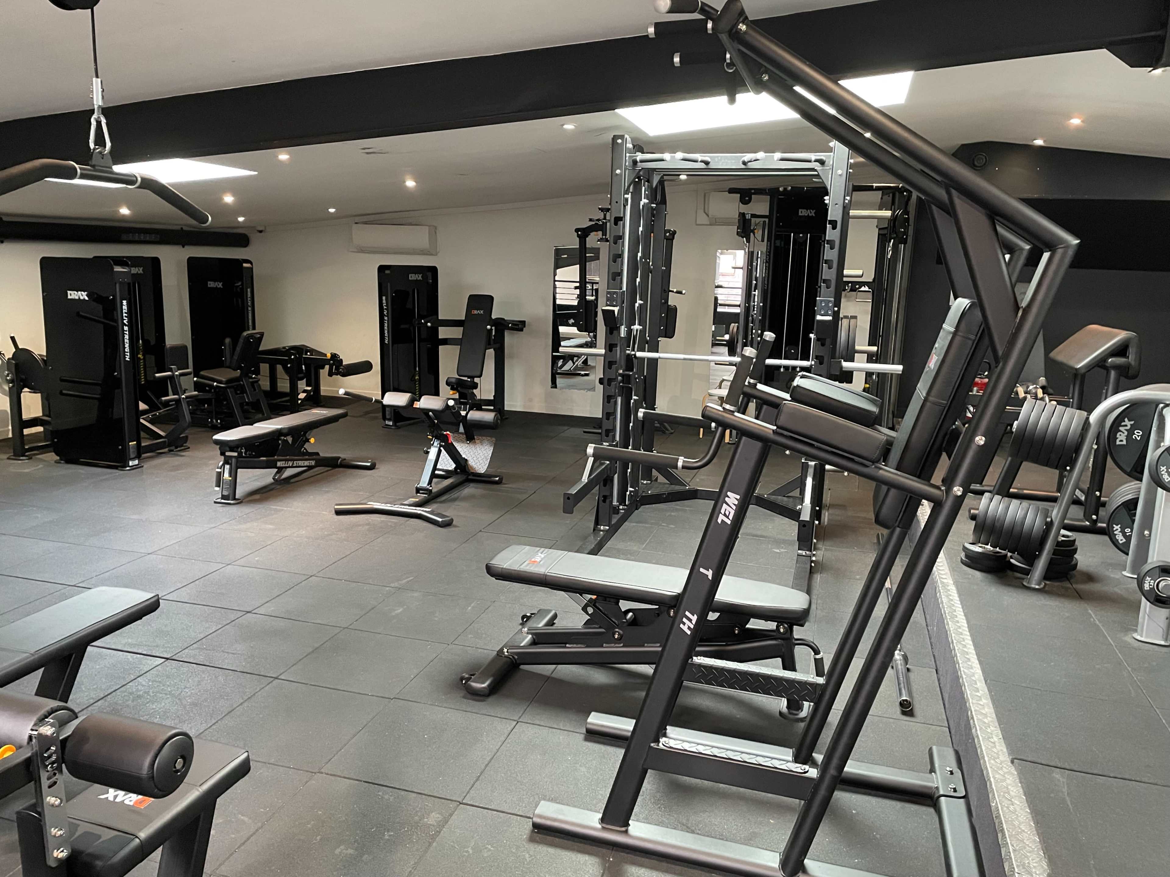 A well-equipped gym with various exercise machines and weights arranged on a black rubber floor.