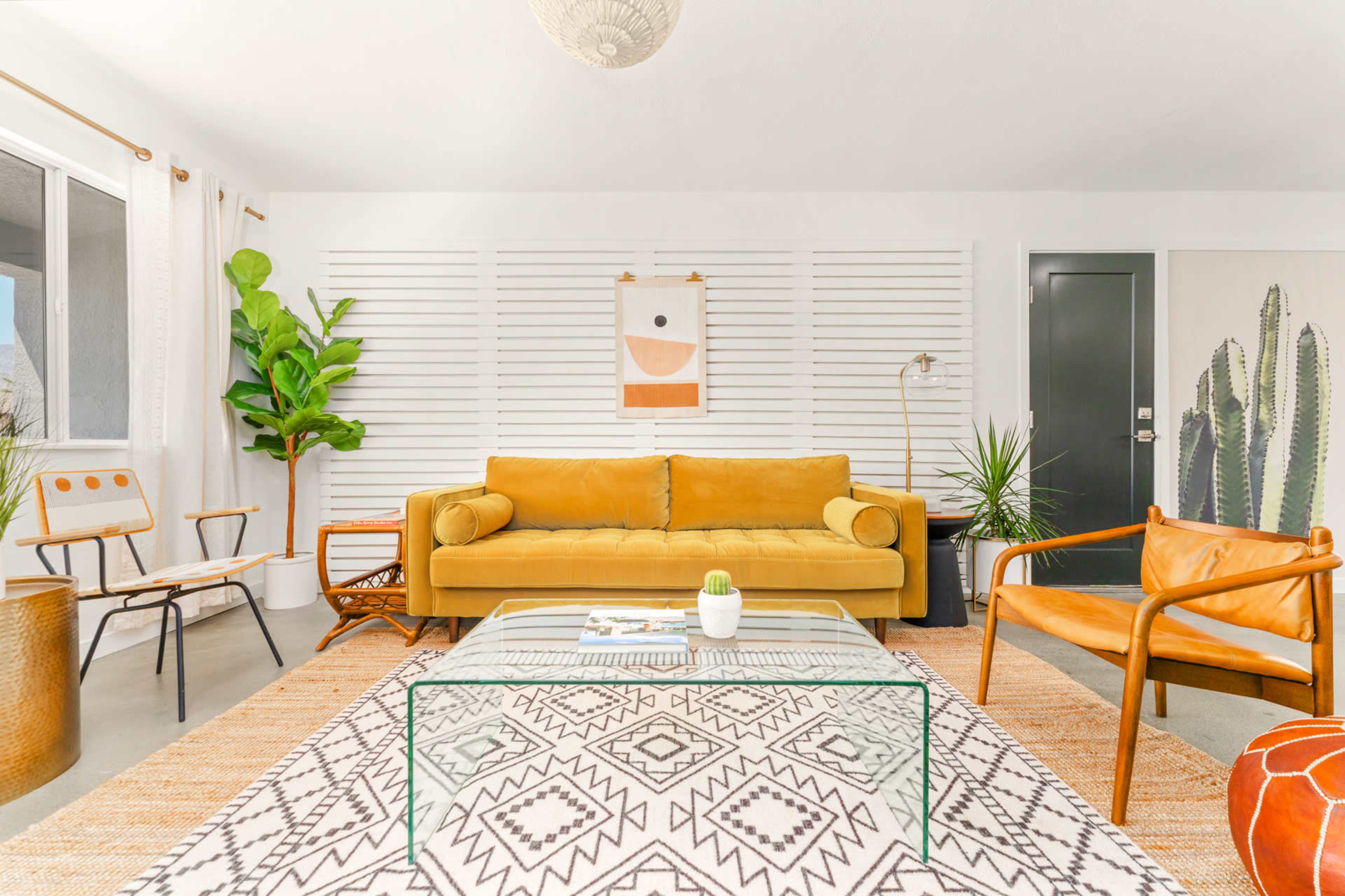 A bright, modern dining area with a large wooden table surrounded by chairs and potted plants in the background.