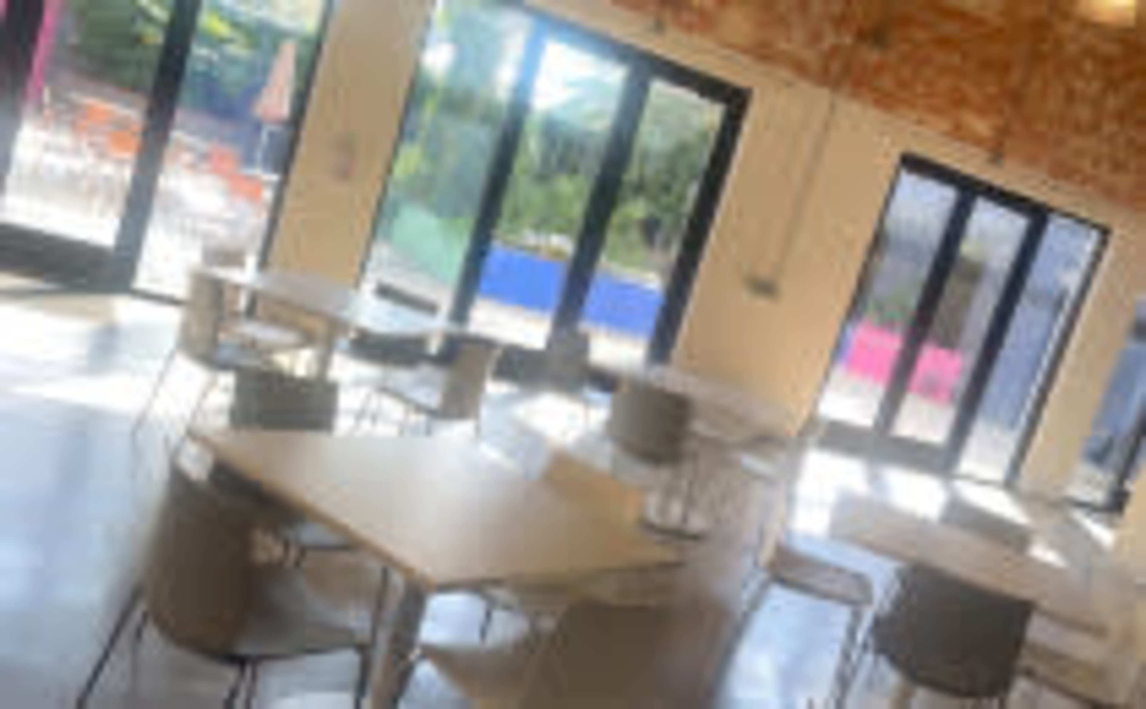 A bright, modern dining area with several tables and chairs, large windows, and a view of an outdoor space.