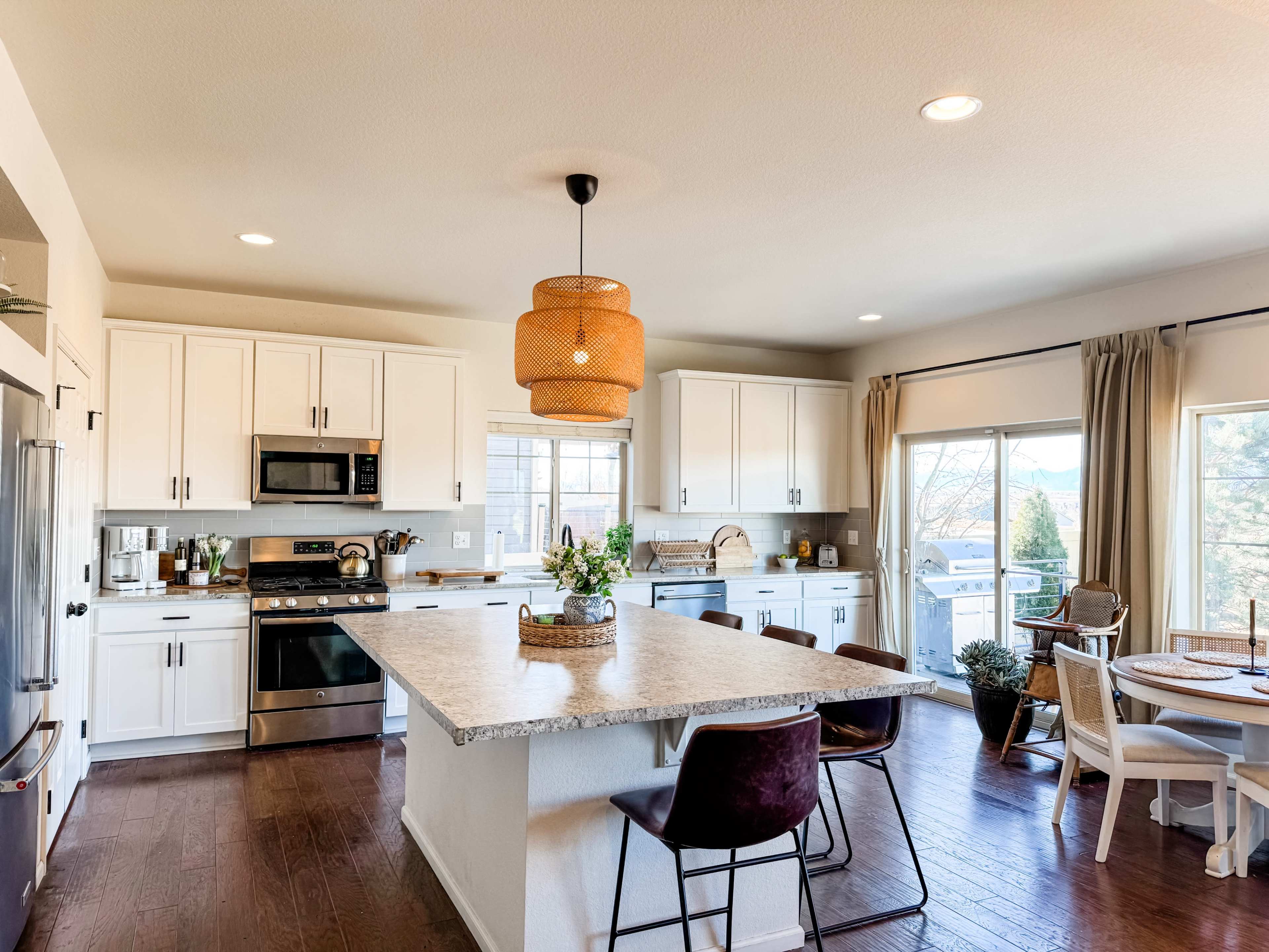 The image shows a modern kitchen with white cabinetry, a large island, and a dining area featuring a round table and chairs.