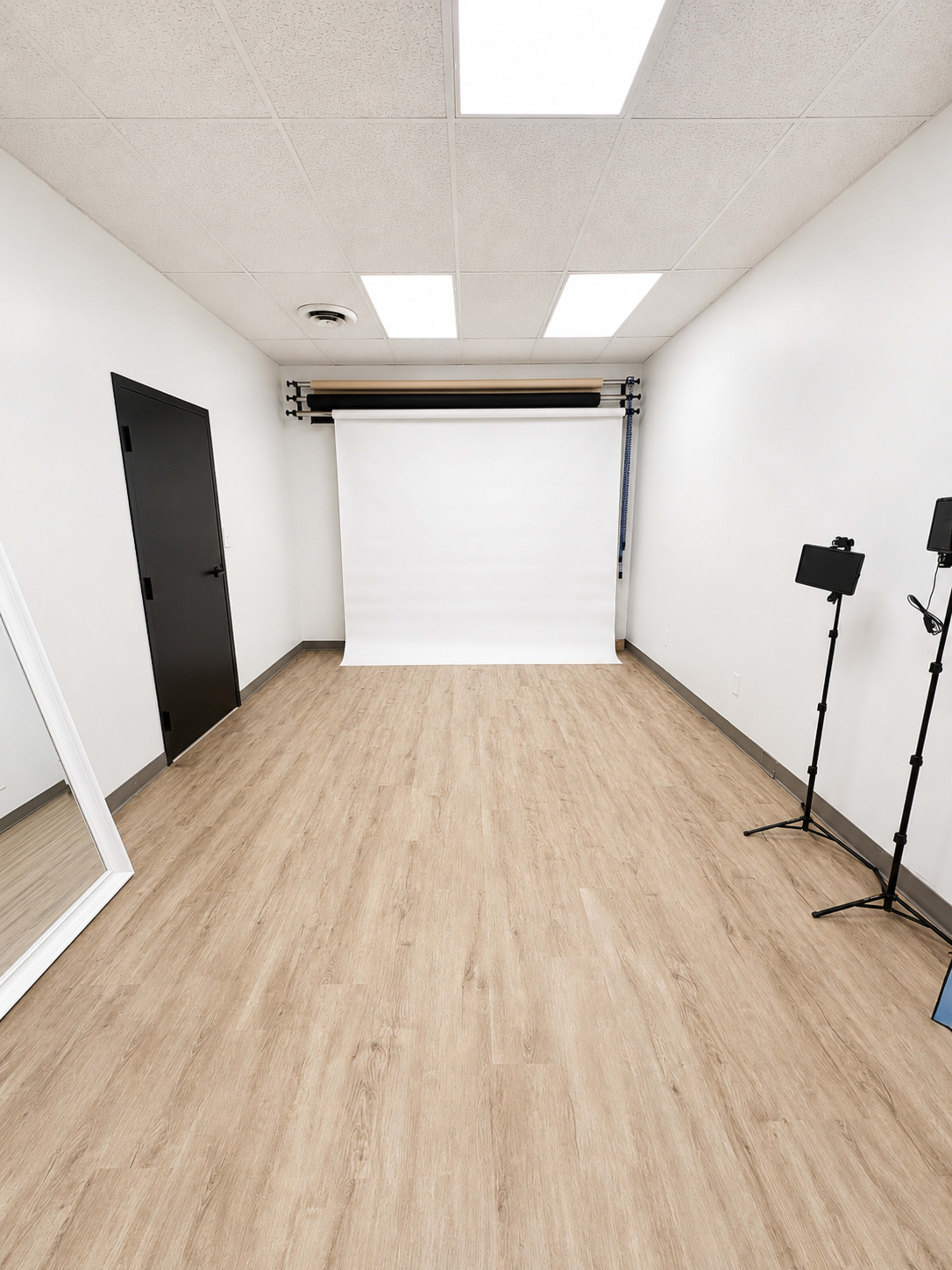 The image shows a spacious, well-lit studio with a white backdrop, a full-length mirror, and two light stands on the floor.