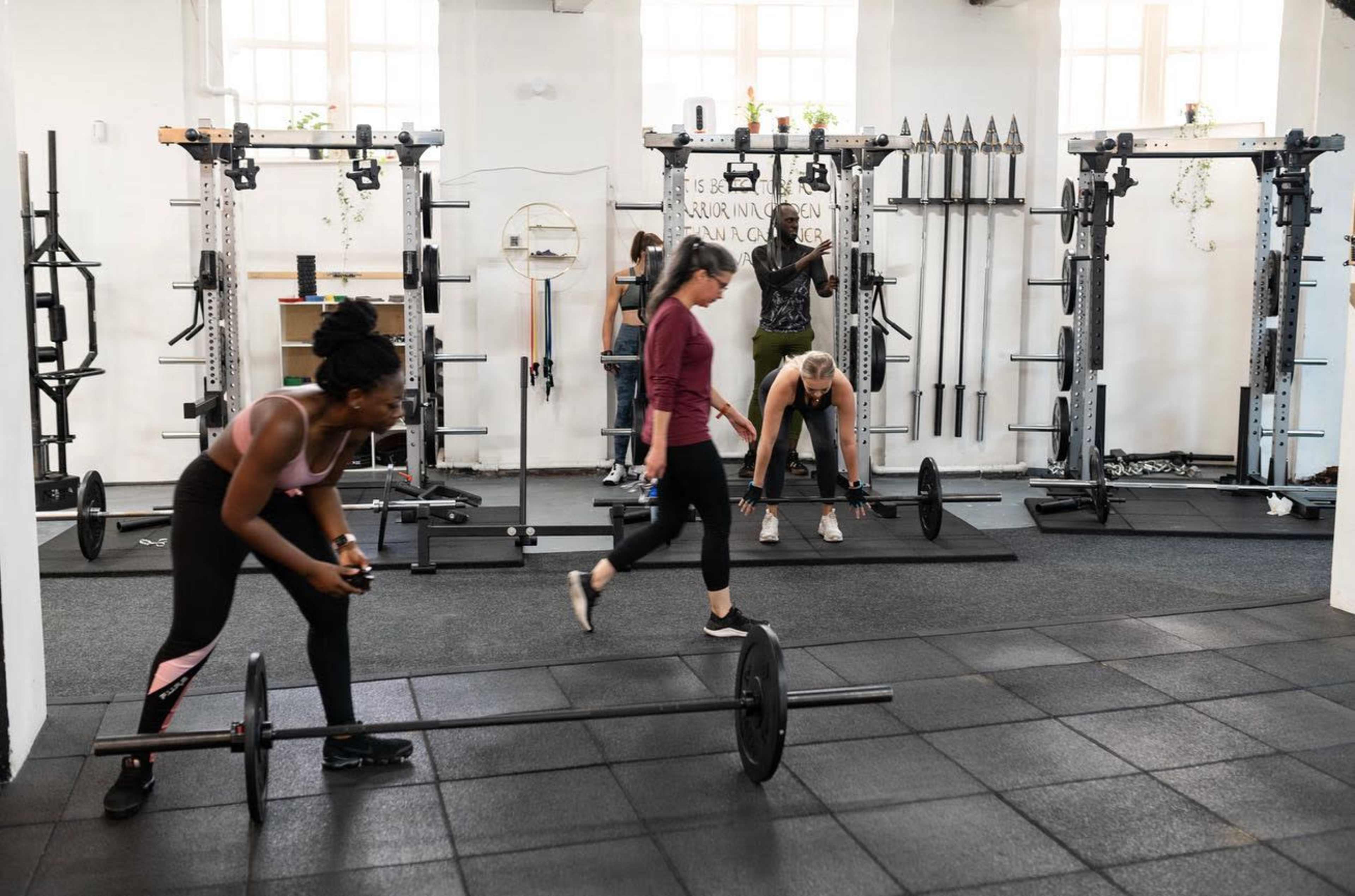 A group of women is working out in a gym with weightlifting equipment and exercise mats.