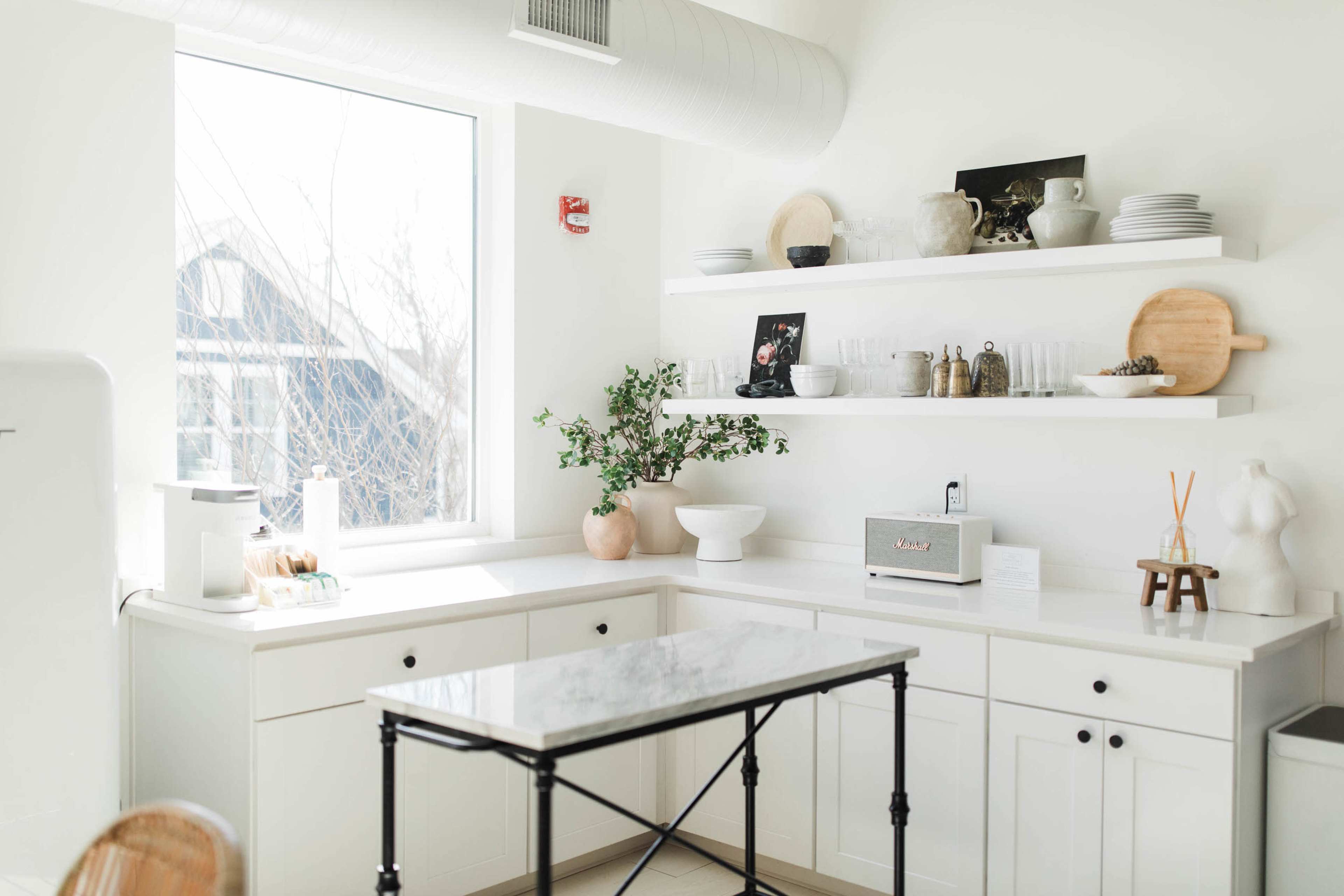 A bright kitchen features white cabinetry, a marble countertop, and open shelves displaying dishware and decor.