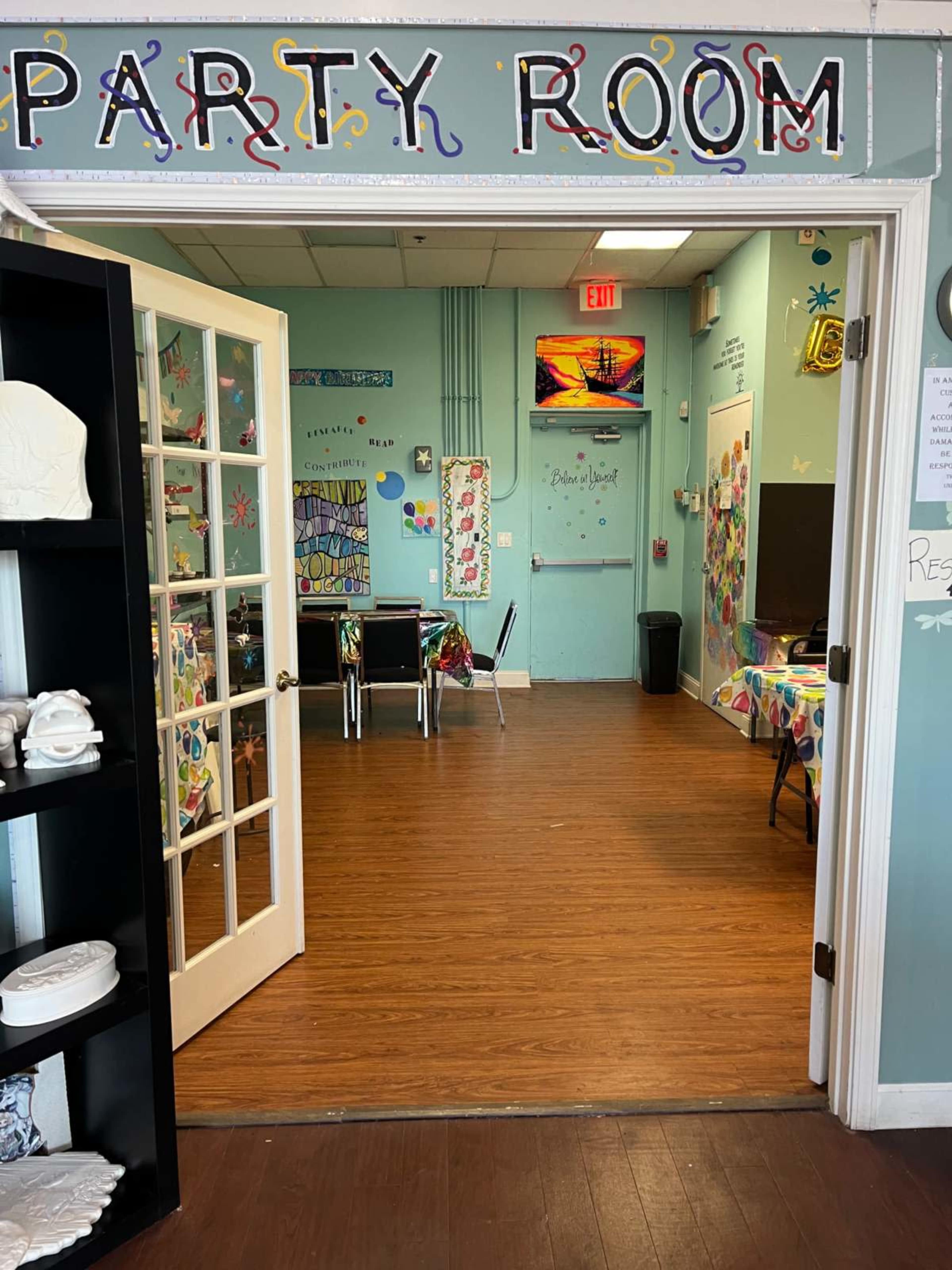 The entrance to a brightly decorated party room with tables, chairs, and colorful artwork on the walls.