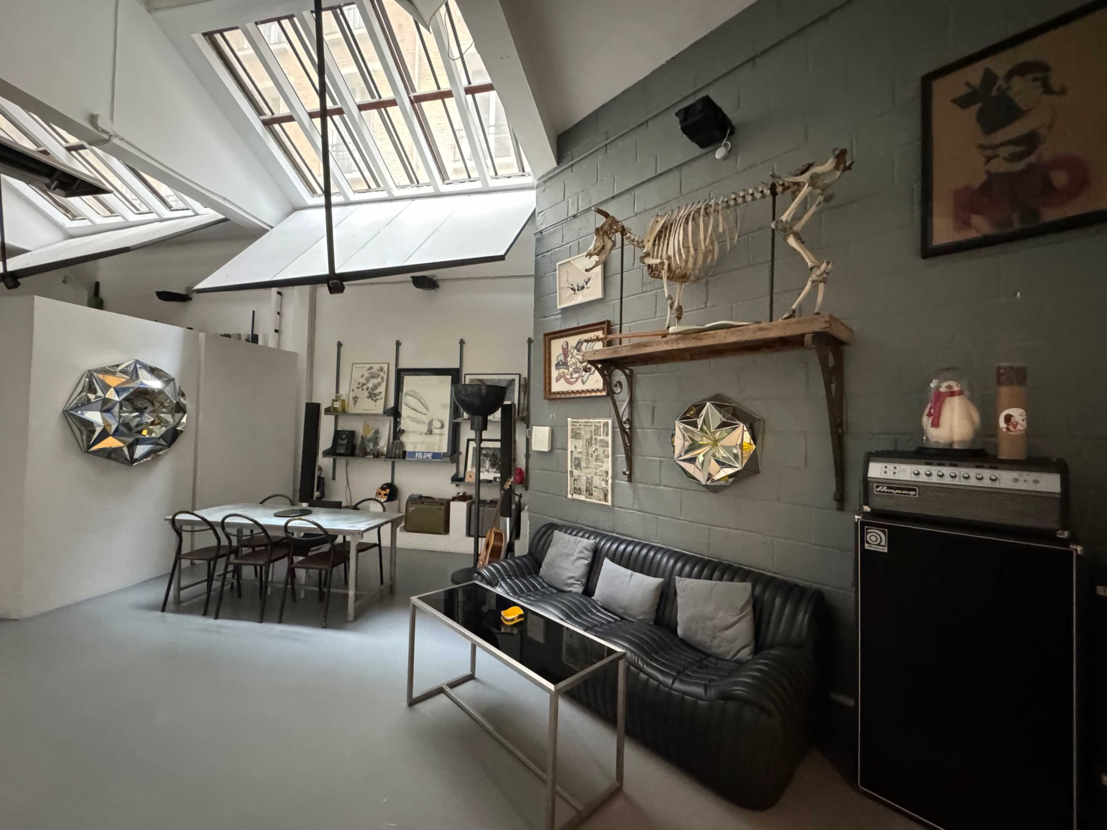 The image shows an industrial-style room featuring a black leather sofa, a glass coffee table, and wall decorations including a skeleton of a horse mounted on a wooden shelf.