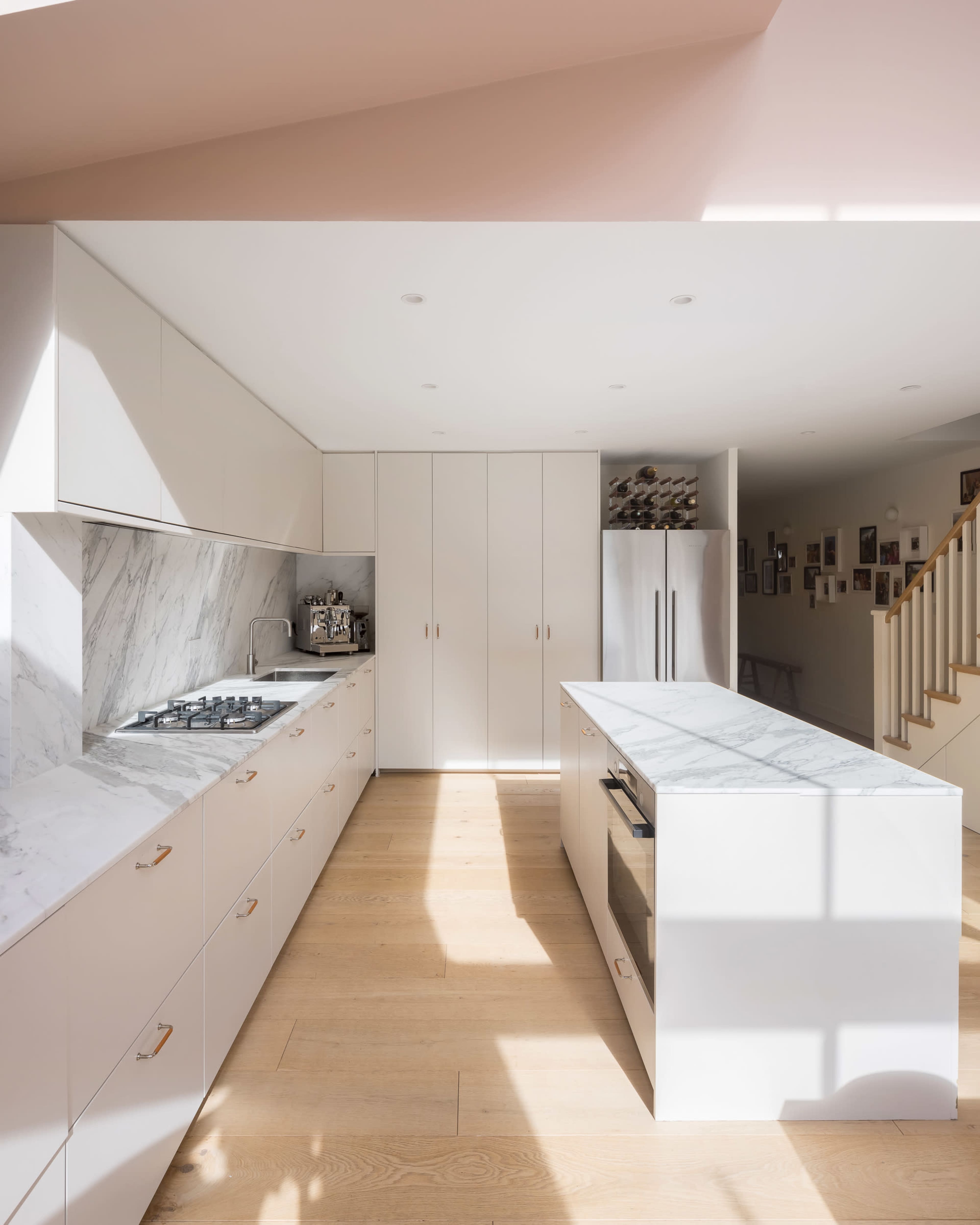 A modern kitchen features white cabinetry, a marble backsplash, and an island with a marble countertop, illuminated by natural light.