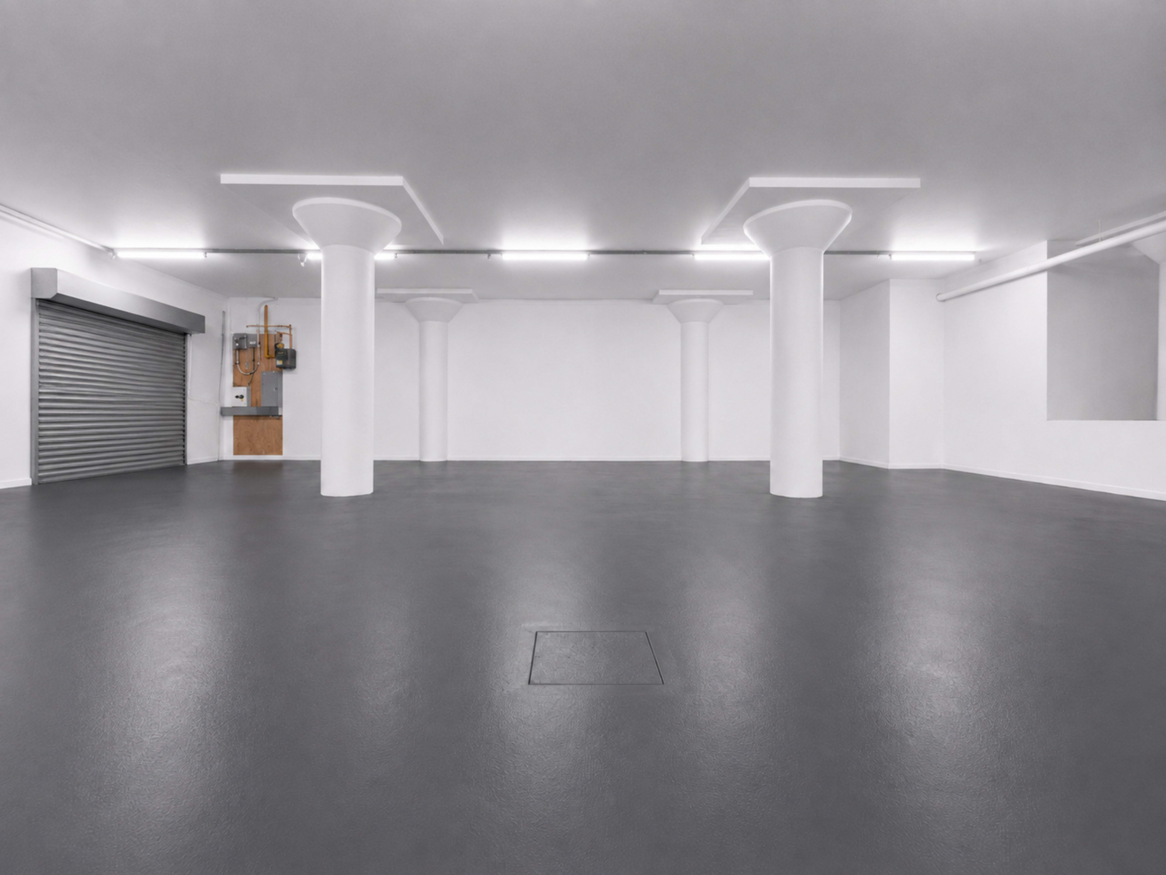 The image shows a spacious, empty indoor garage with polished gray floors and several white columns supporting the ceiling.
