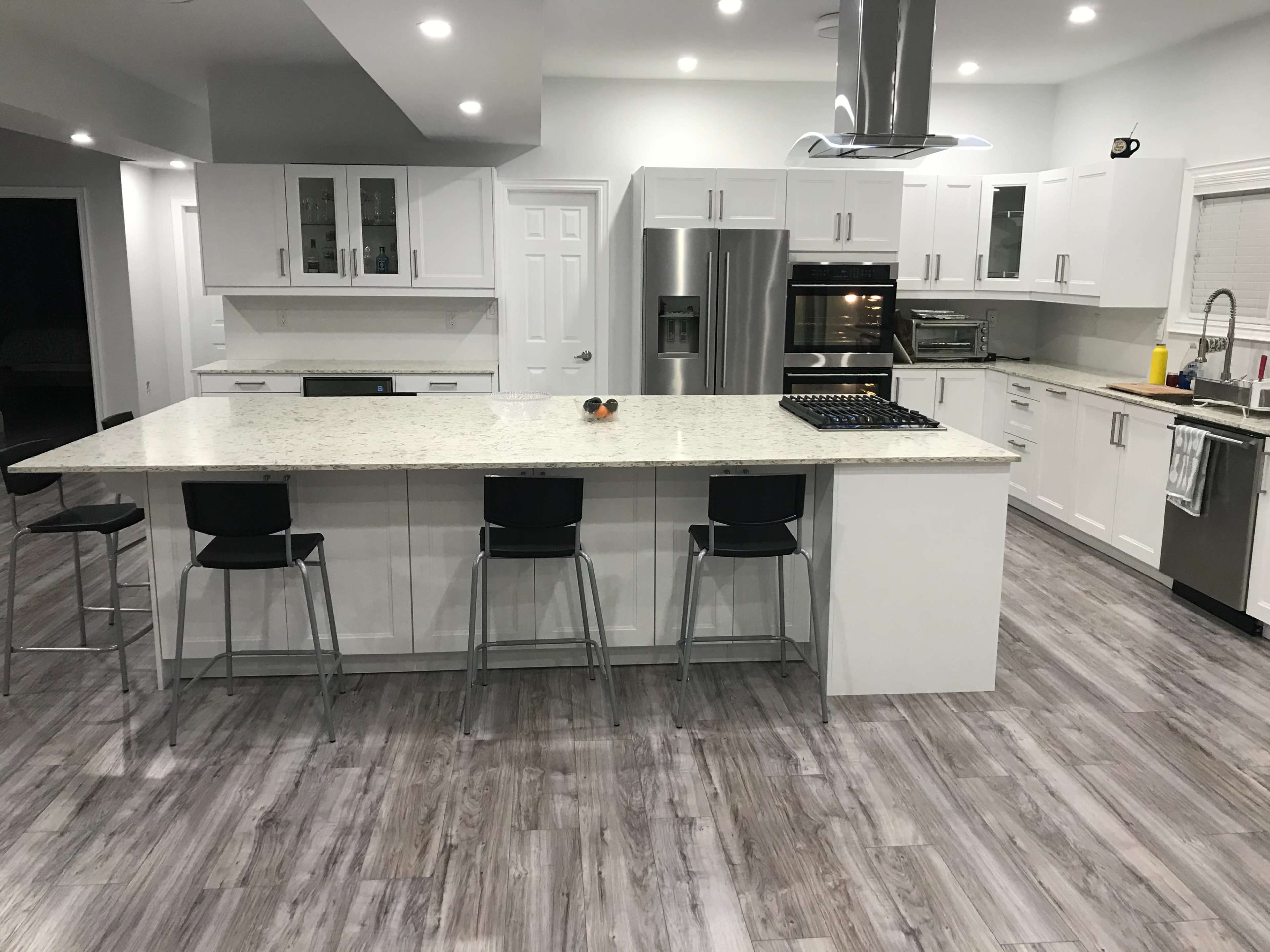 A modern kitchen with white cabinets, a large island with seating, stainless steel appliances, and light wood flooring.