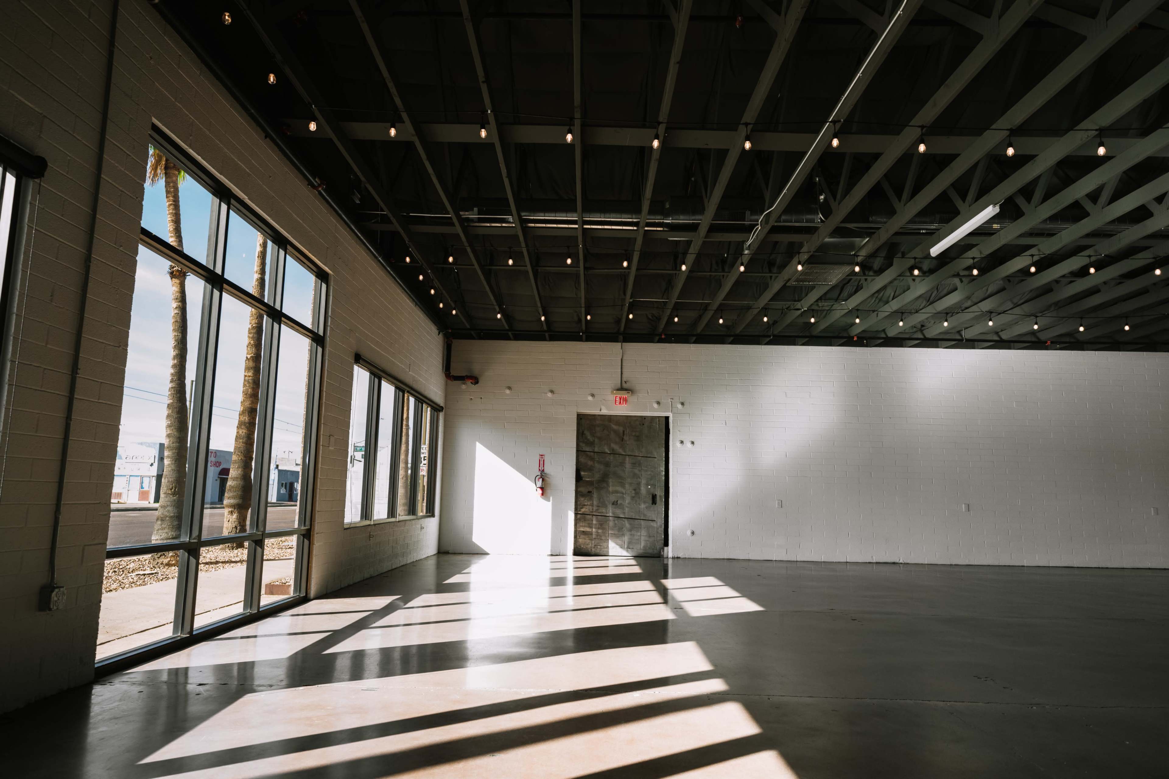 The image shows a spacious, empty room with large windows allowing light to cast shadows on the concrete floor.