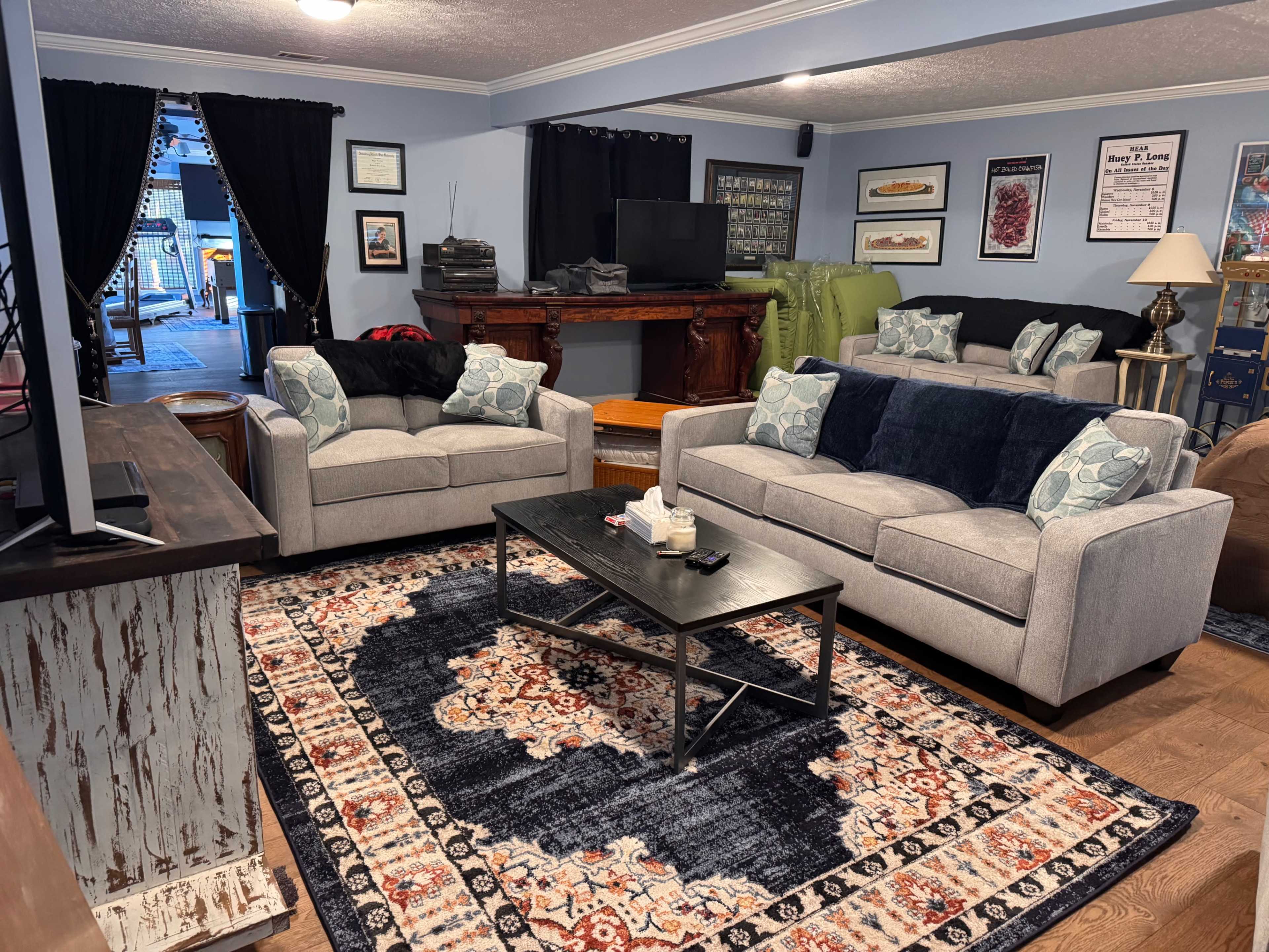 A spacious living room features two gray sofas adorned with blue and white cushions, a dark coffee table on a decorative rug, and a television set against a wall with framed artwork.