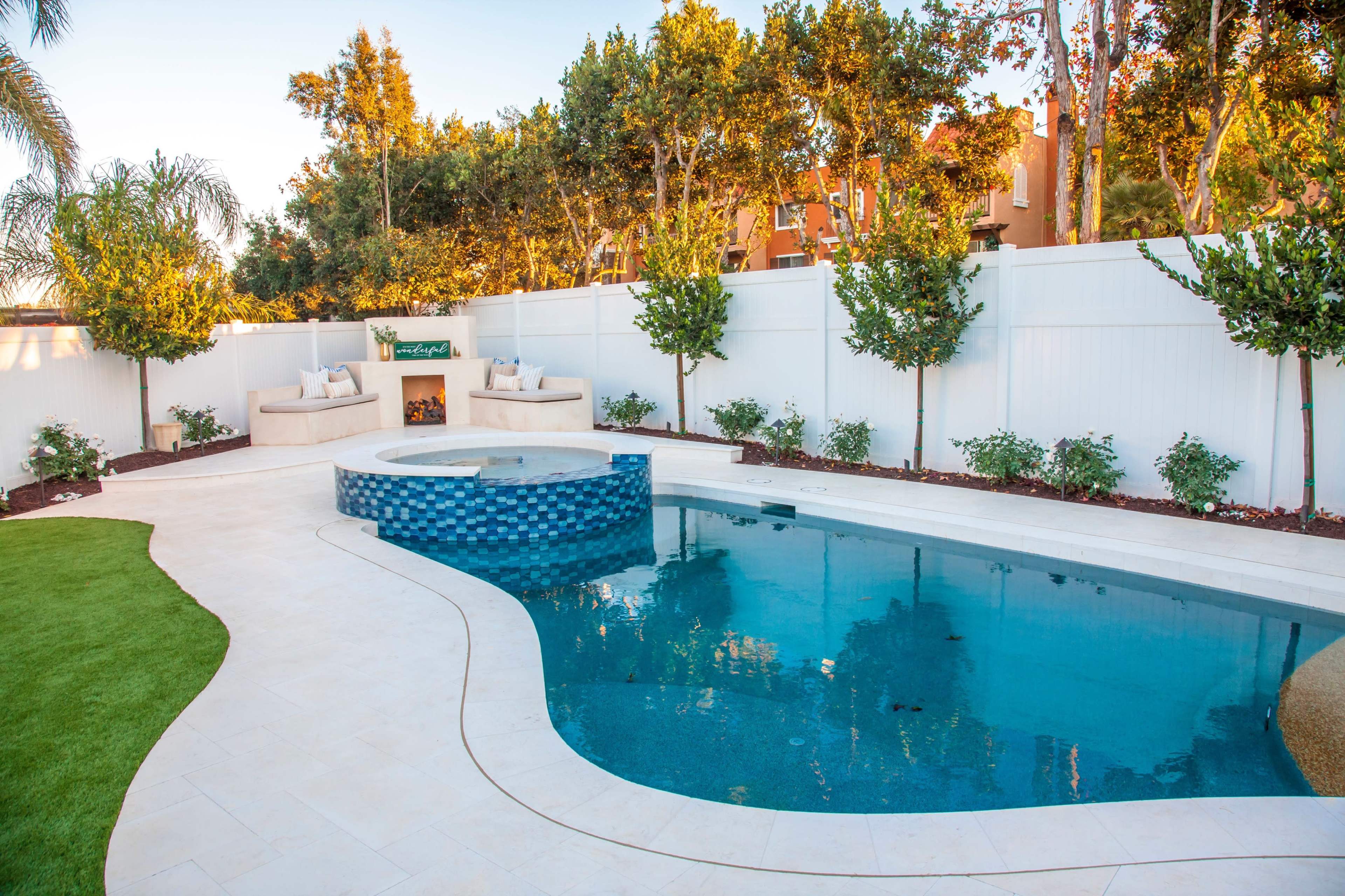 A backyard features a curved swimming pool with blue tiles, a spa area, and landscaped surroundings with lush greenery and seating.