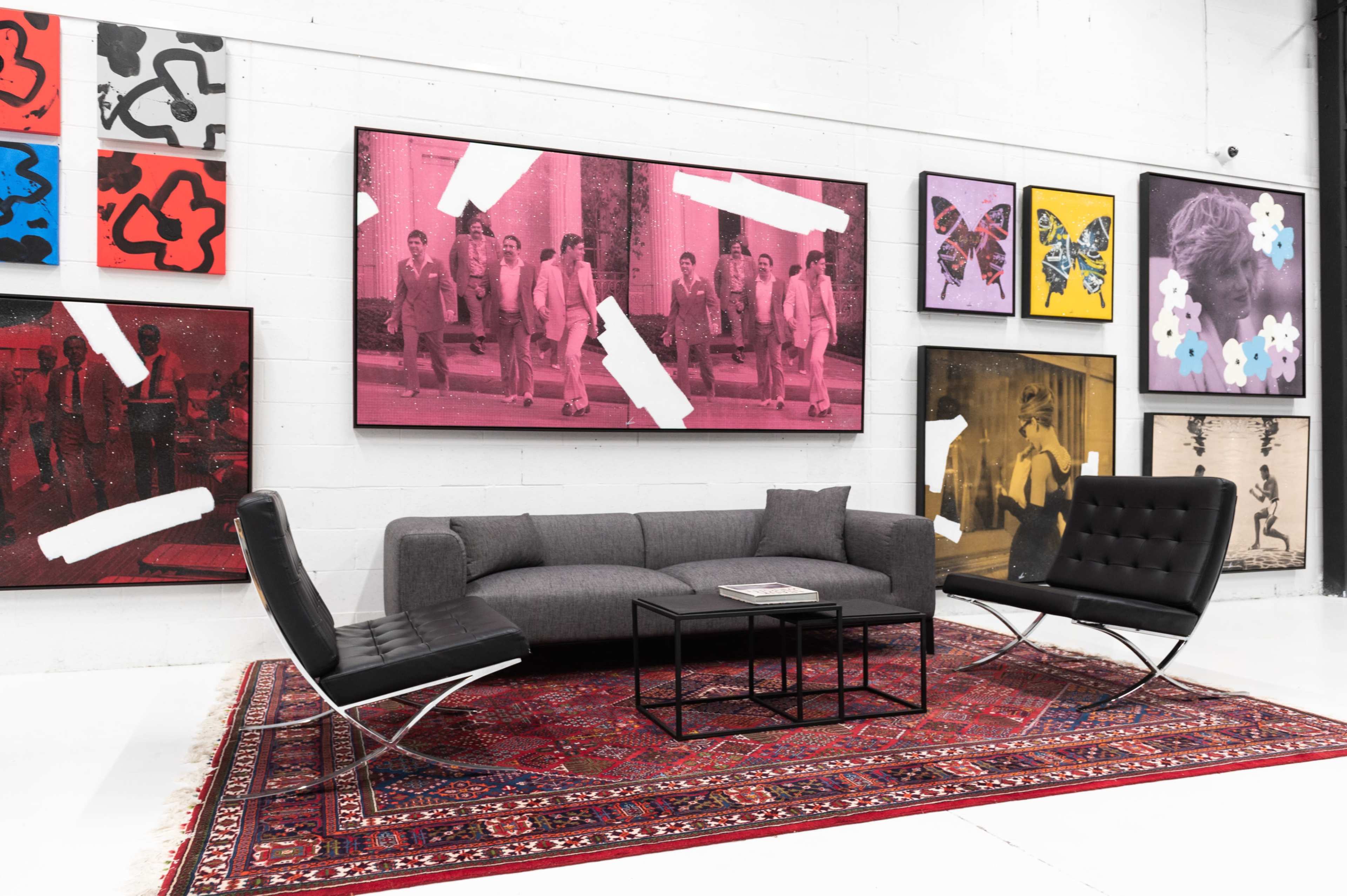 A modern living space featuring a gray sofa, two black chairs, a coffee table, and an array of framed art on the walls.