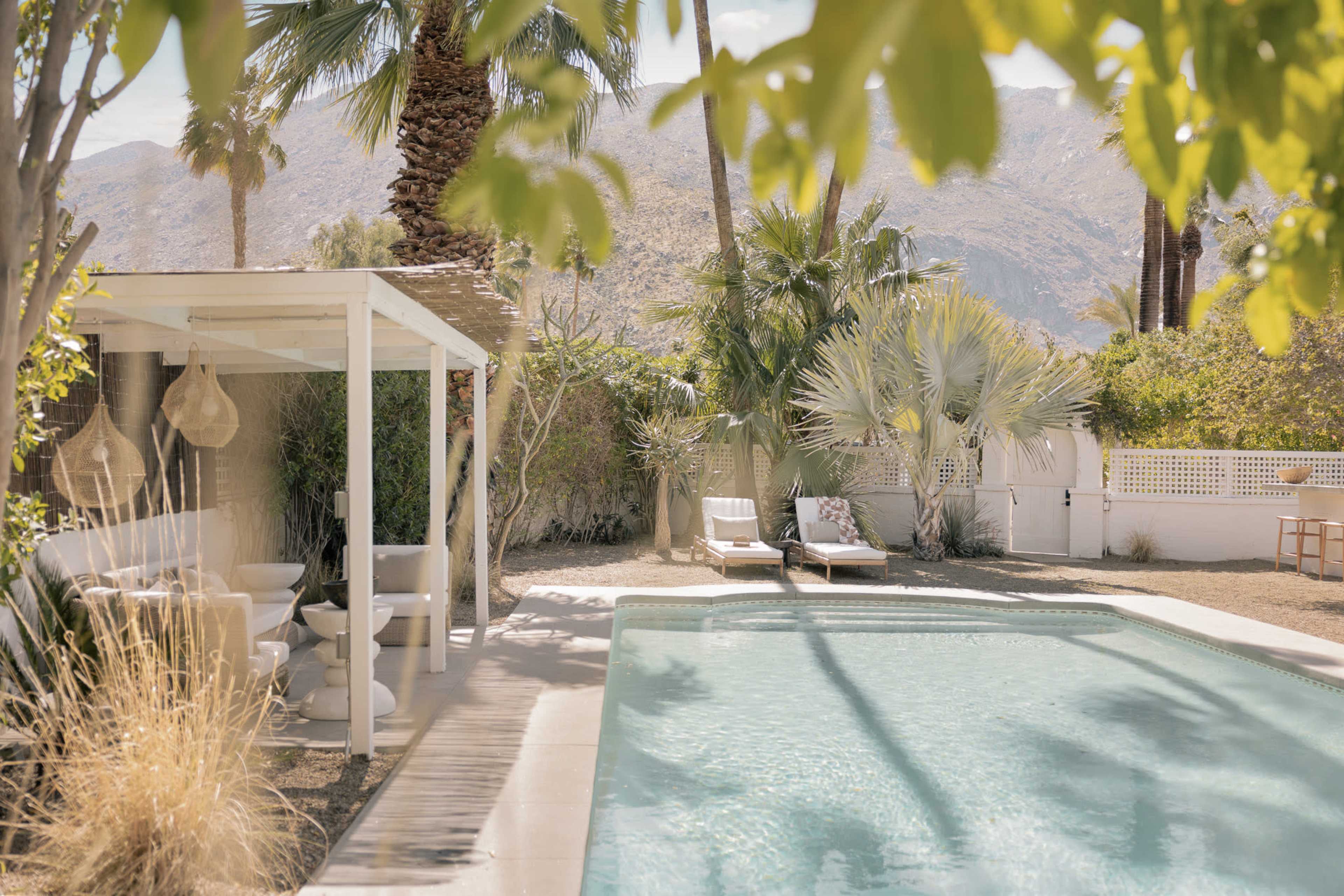 A serene outdoor pool area surrounded by palm trees and lush greenery, with lounge chairs and a shaded structure nearby.