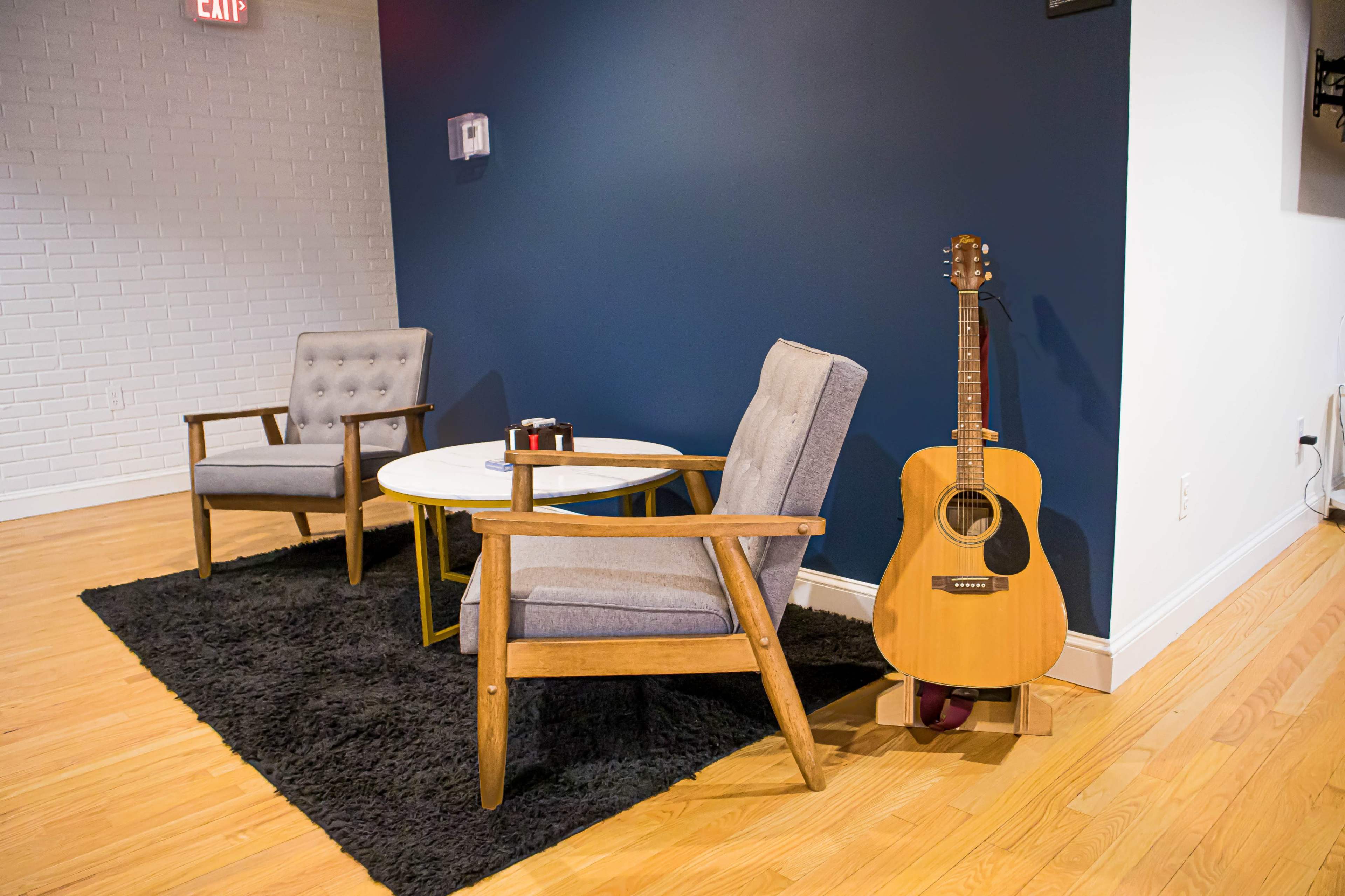 Two wooden chairs are positioned next to a small round table on a black rug, with an acoustic guitar leaning against the wall.