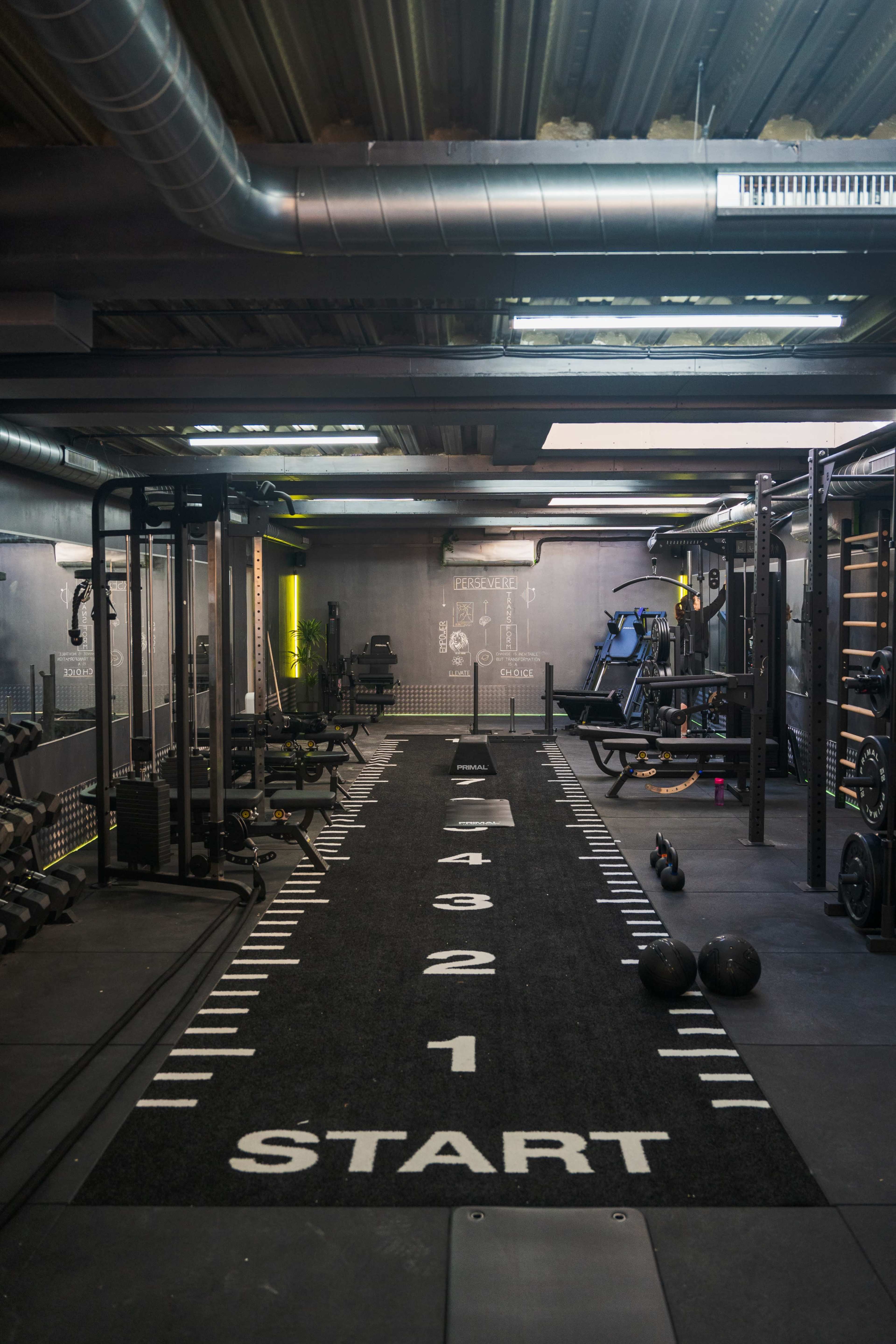 A modern gym with various workout equipment arranged around a track marked with "START" and numbered lines.