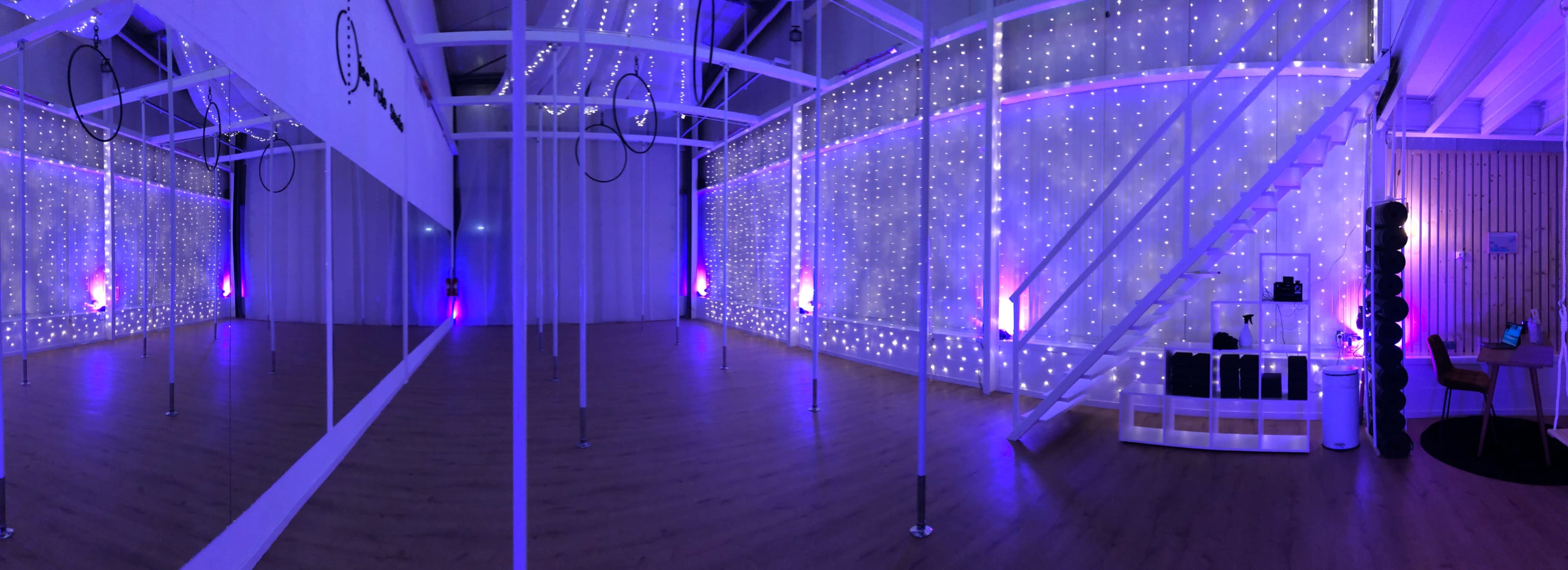 A spacious studio with white walls and wooden floors, illuminated by purple lights and decorated with string lights.