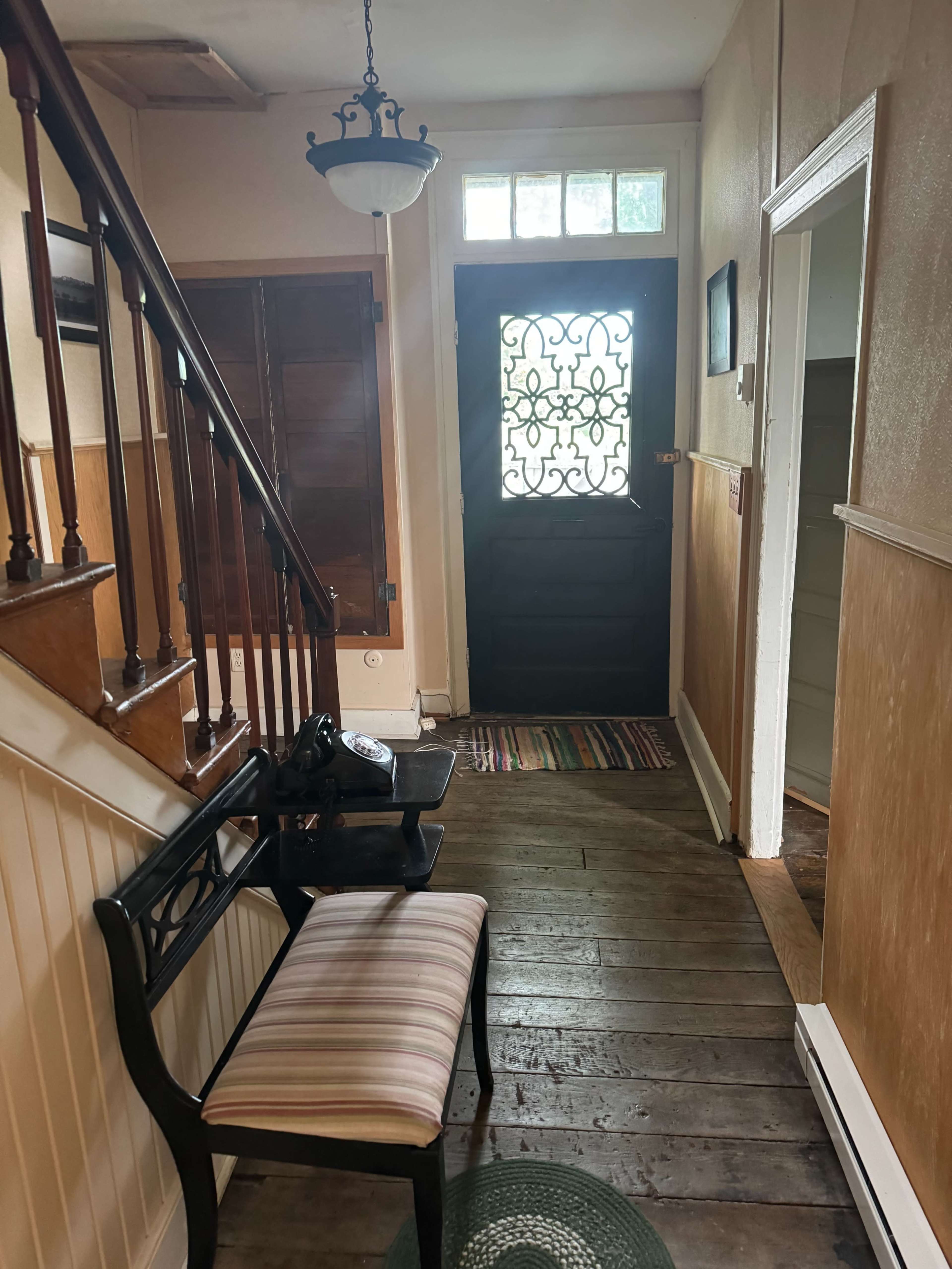 An interior hallway with a staircase, a bench, and a door decorated with an iron grille.