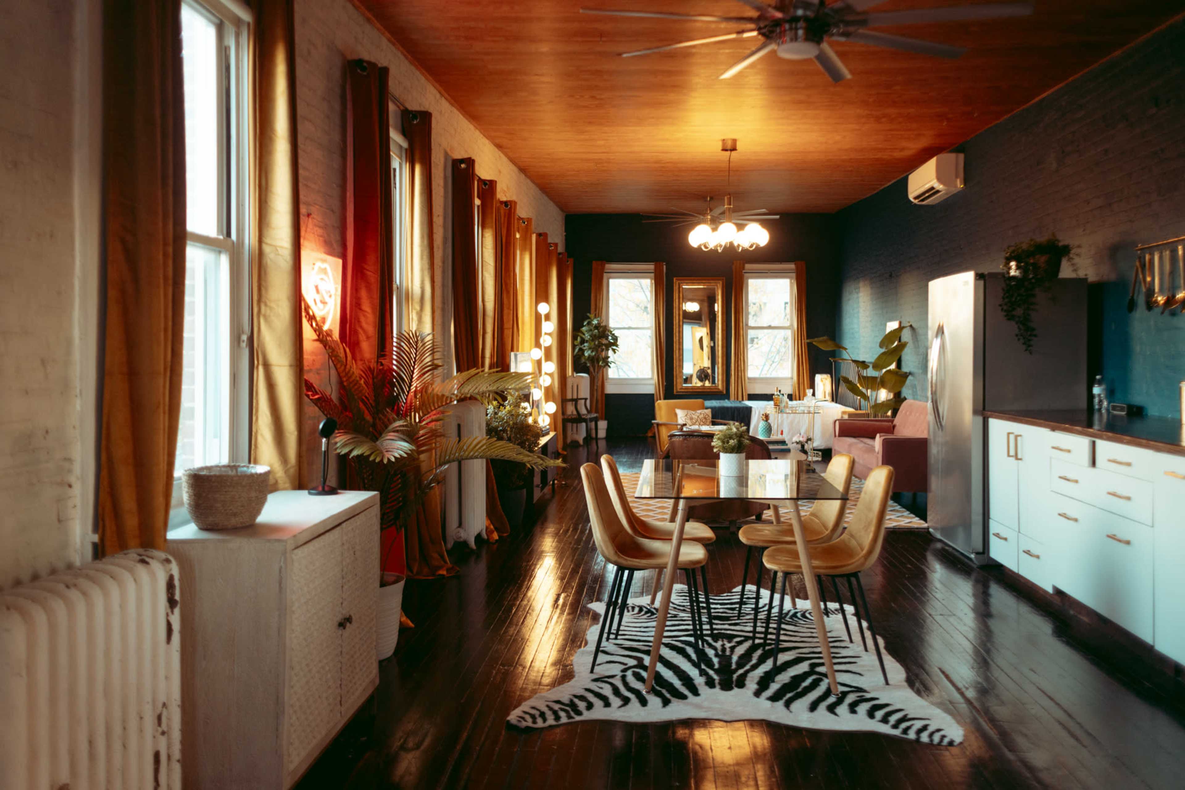 A modern living space with wooden floors, large windows, a dining table, and a blend of contemporary furniture and plants.