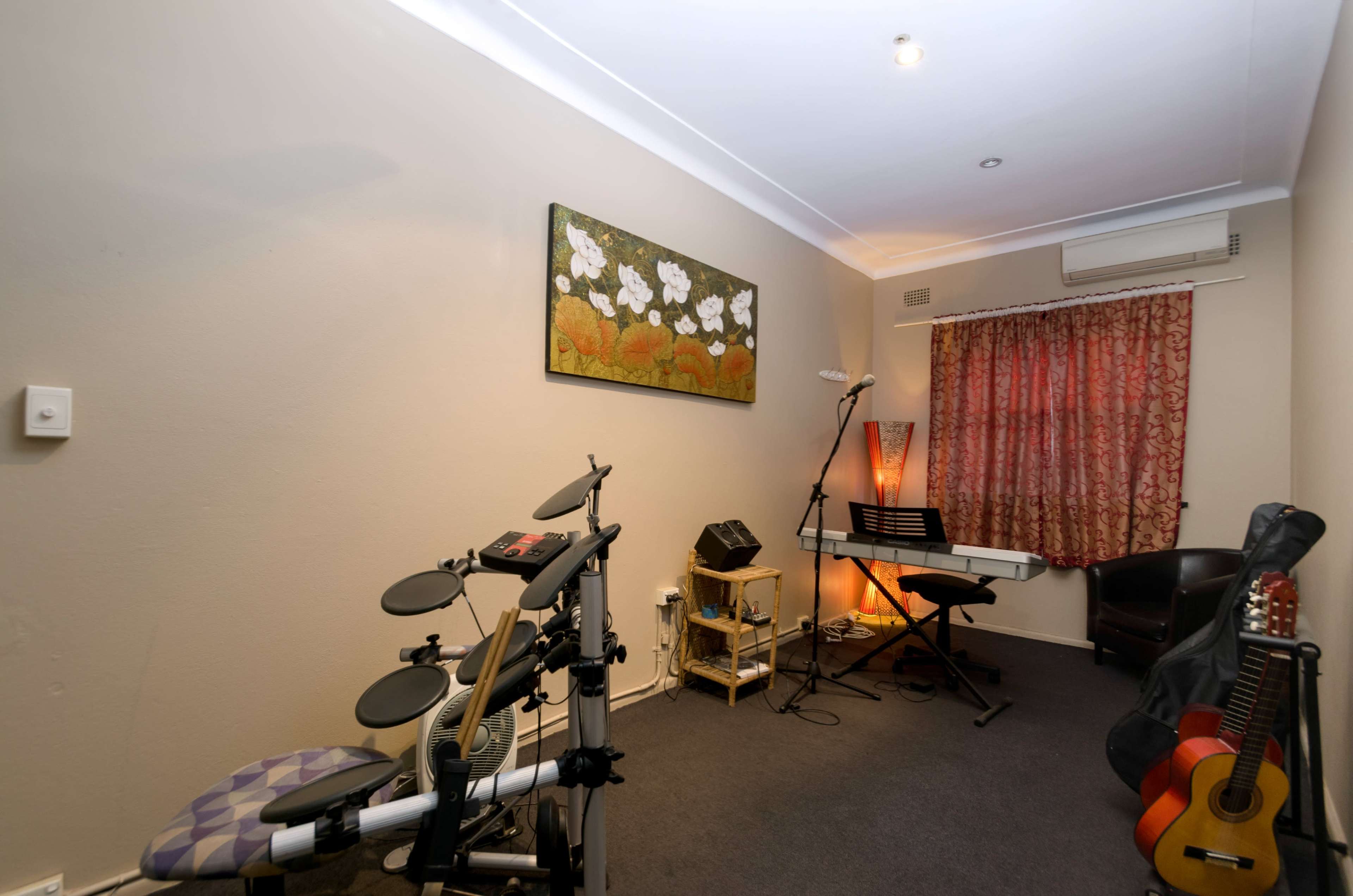 A room contains an electronic drum set, a keyboard on a stand, a chair, and various musical instruments against the wall, with a decorative painting and curtains.