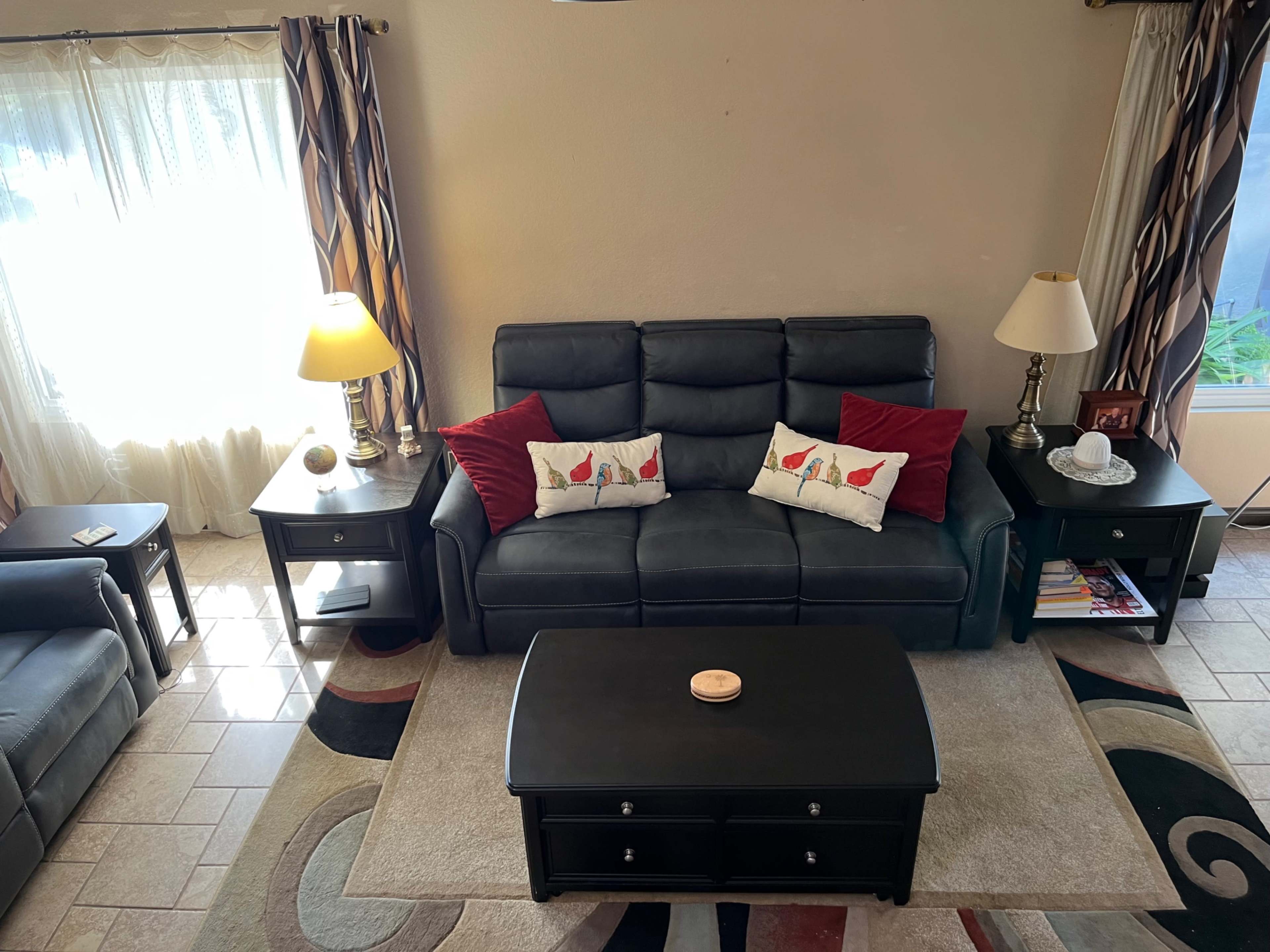 The living room features a gray leather sofa with red pillows, a dark coffee table, and a lamp beside a window with sheer curtains.