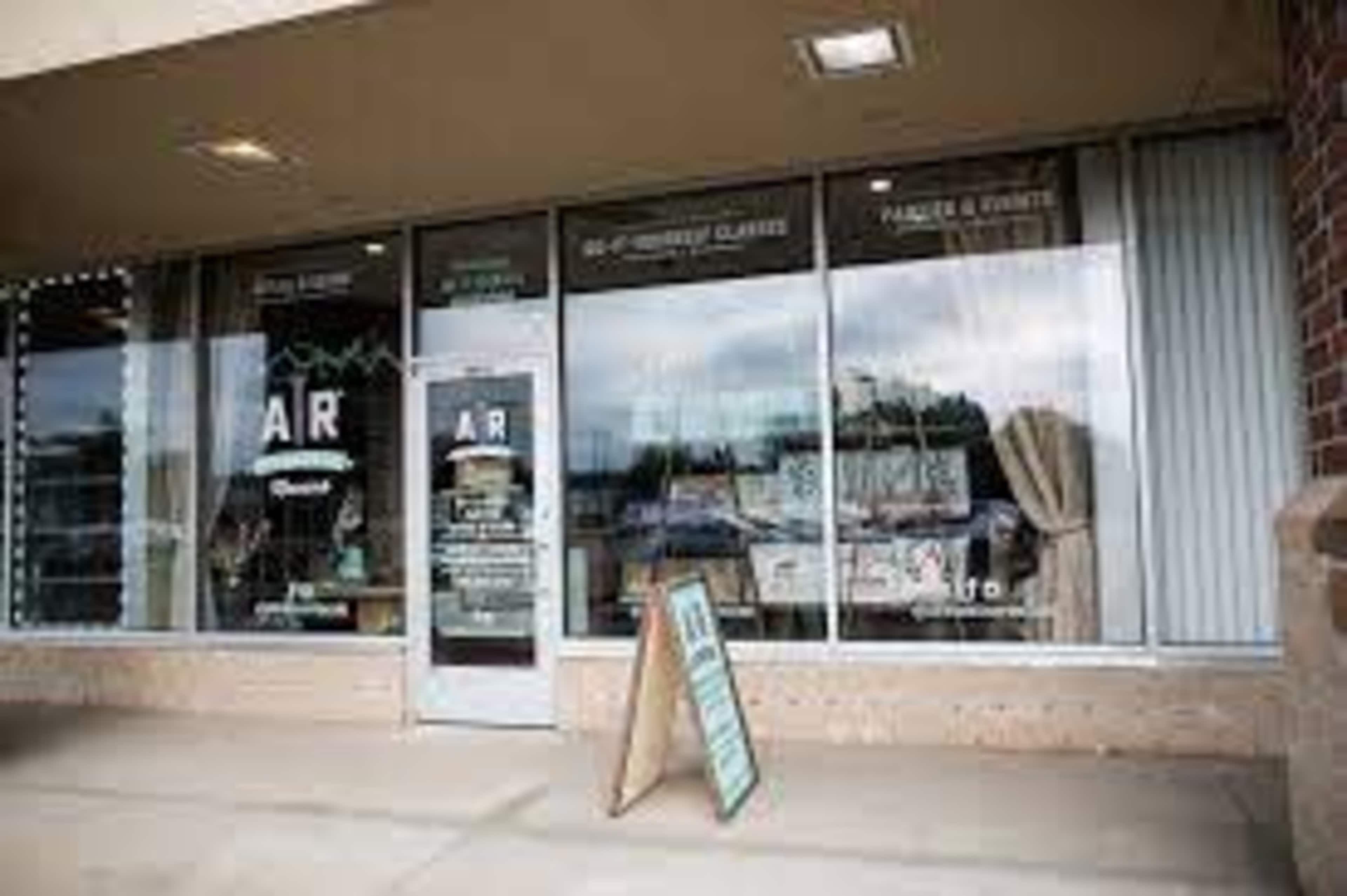 The image shows the storefront of a business with large windows displaying various items and a signboard outside.