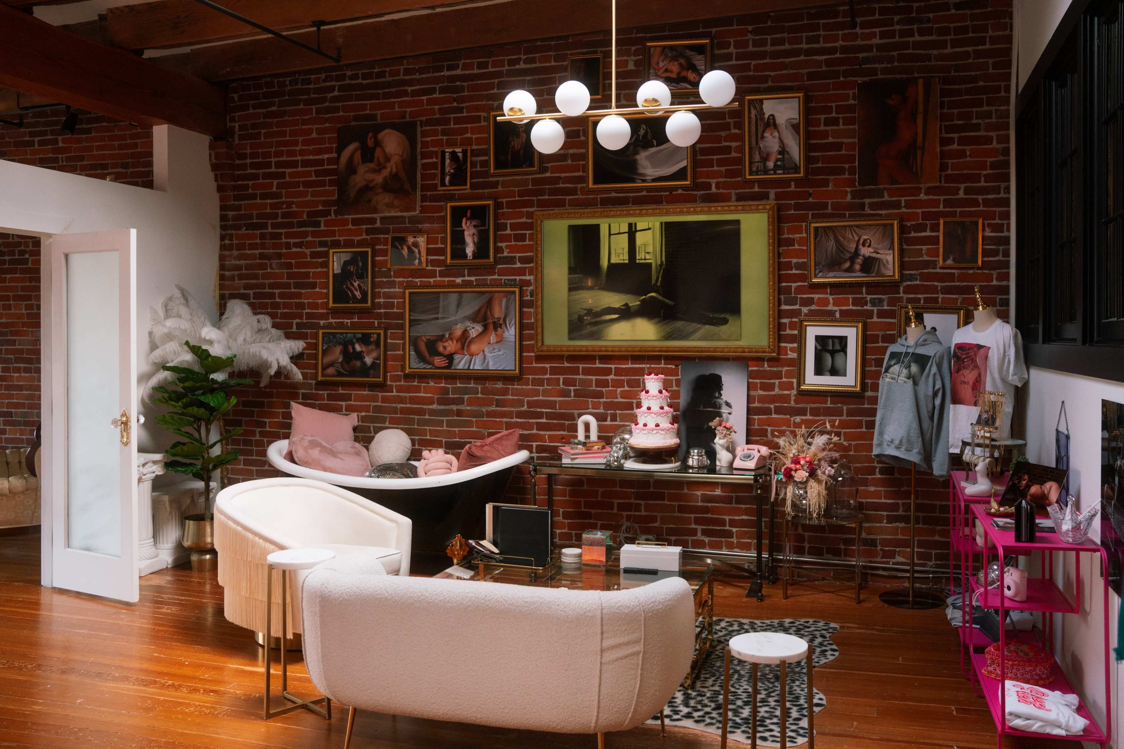 The image shows a stylish living room featuring a brick wall adorned with framed artwork, a modern chandelier, and a decorative cake on a table.