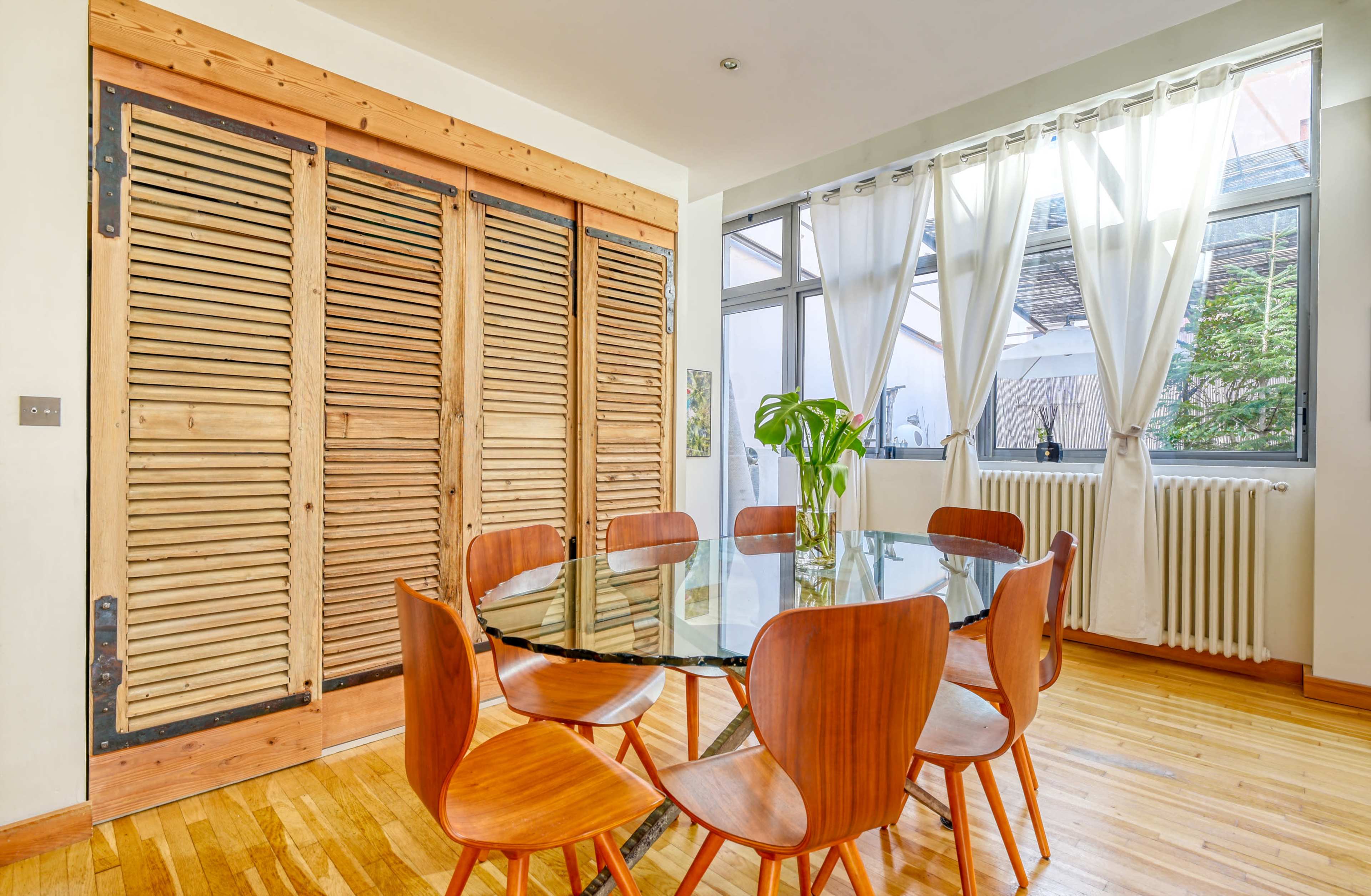 A modern dining area features a round glass table surrounded by wooden chairs, with large windows and wooden sliding doors in the background.