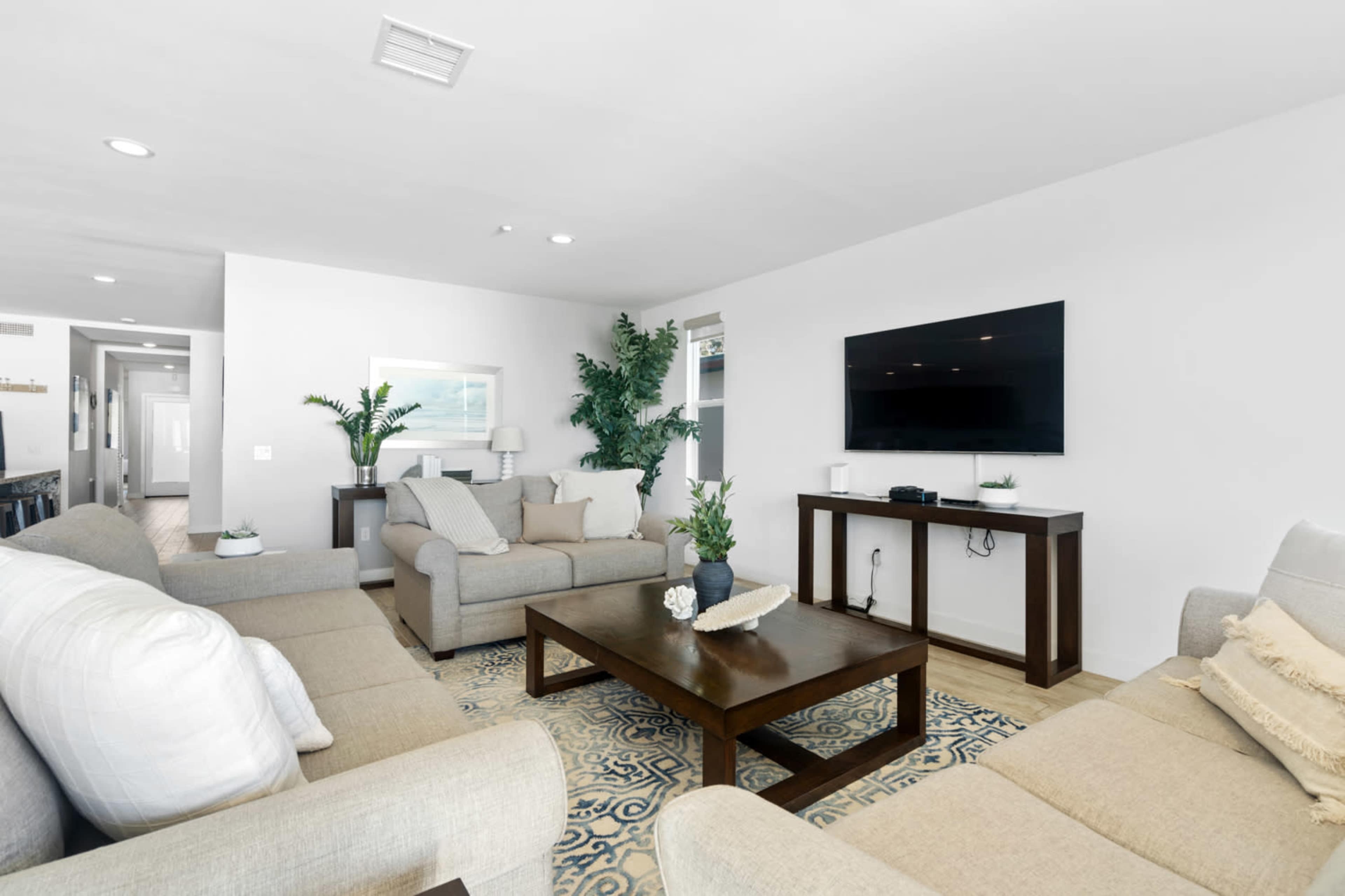 A modern living room with light-colored furnishings, a coffee table, and a wall-mounted television.