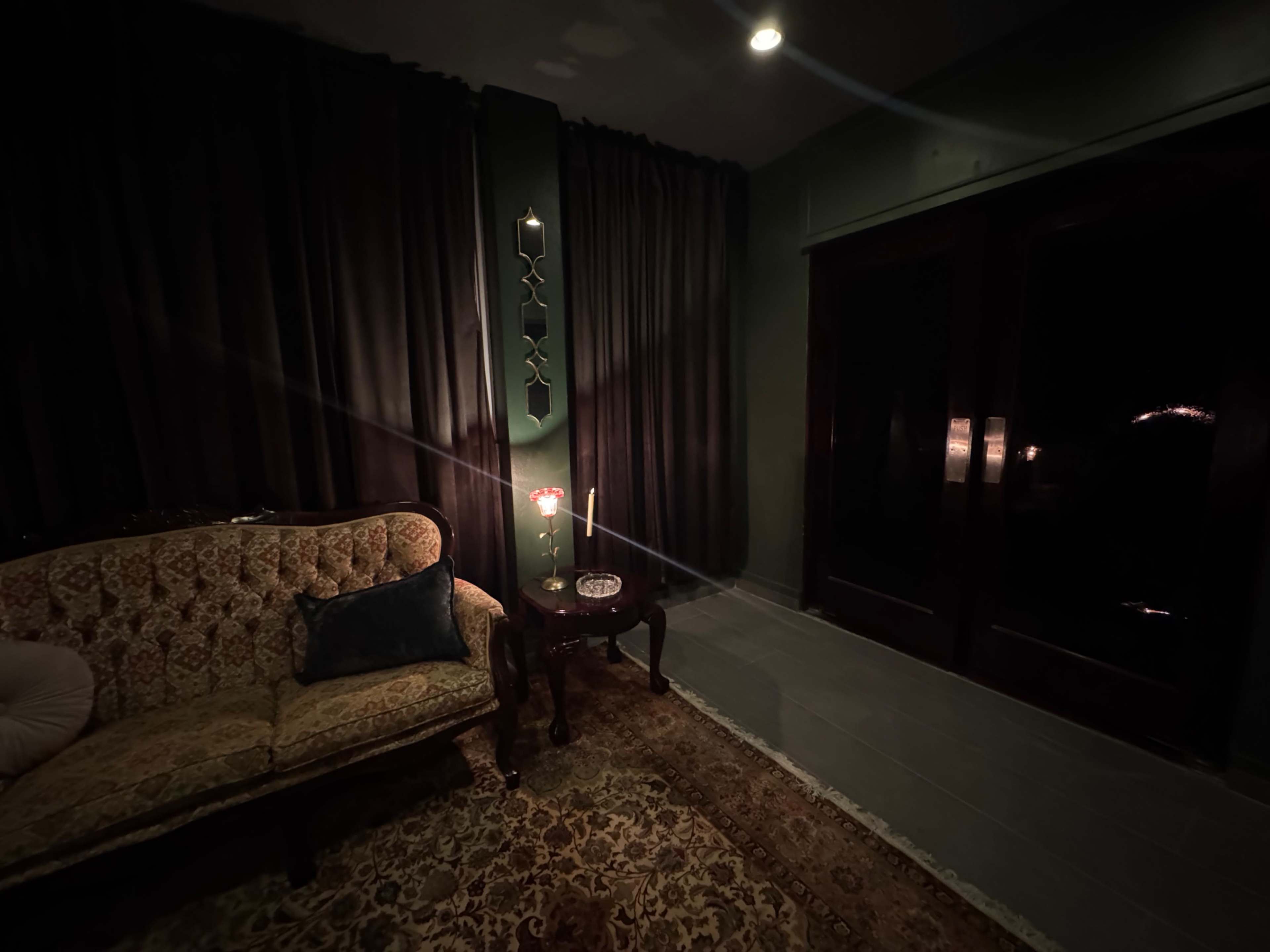 The image shows a dimly lit room with a vintage sofa, a dark curtain, and a small table holding a candle.
