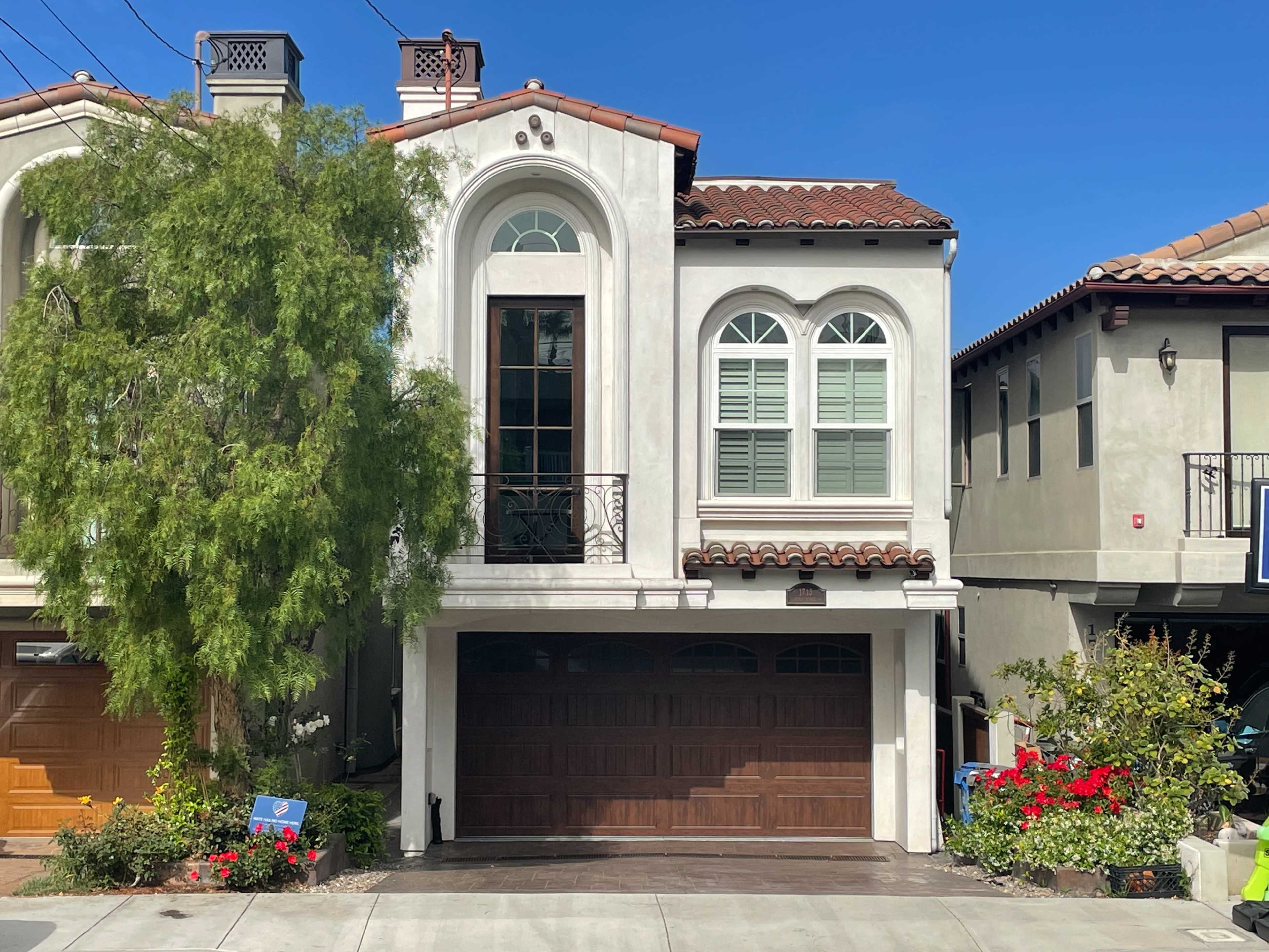 The image shows a two-story residential house with arched windows, a wooden garage door, and a landscaped front yard.