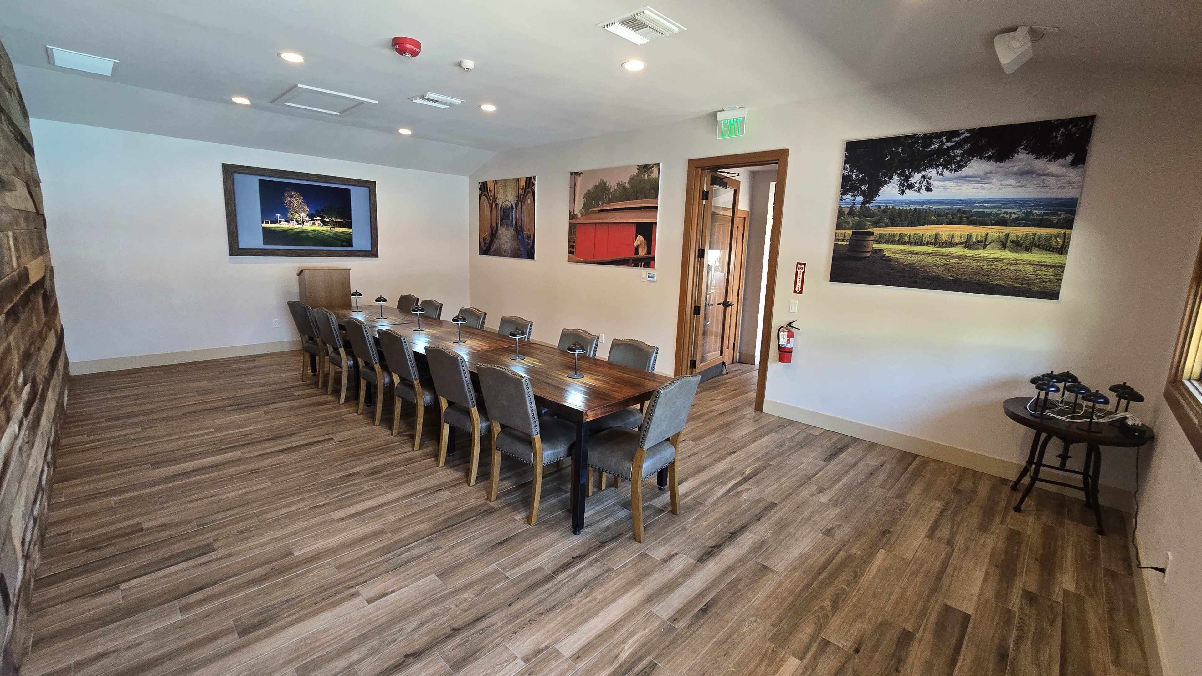 A large conference room features a long wooden table surrounded by chairs, with artwork on the walls and a screen at one end.