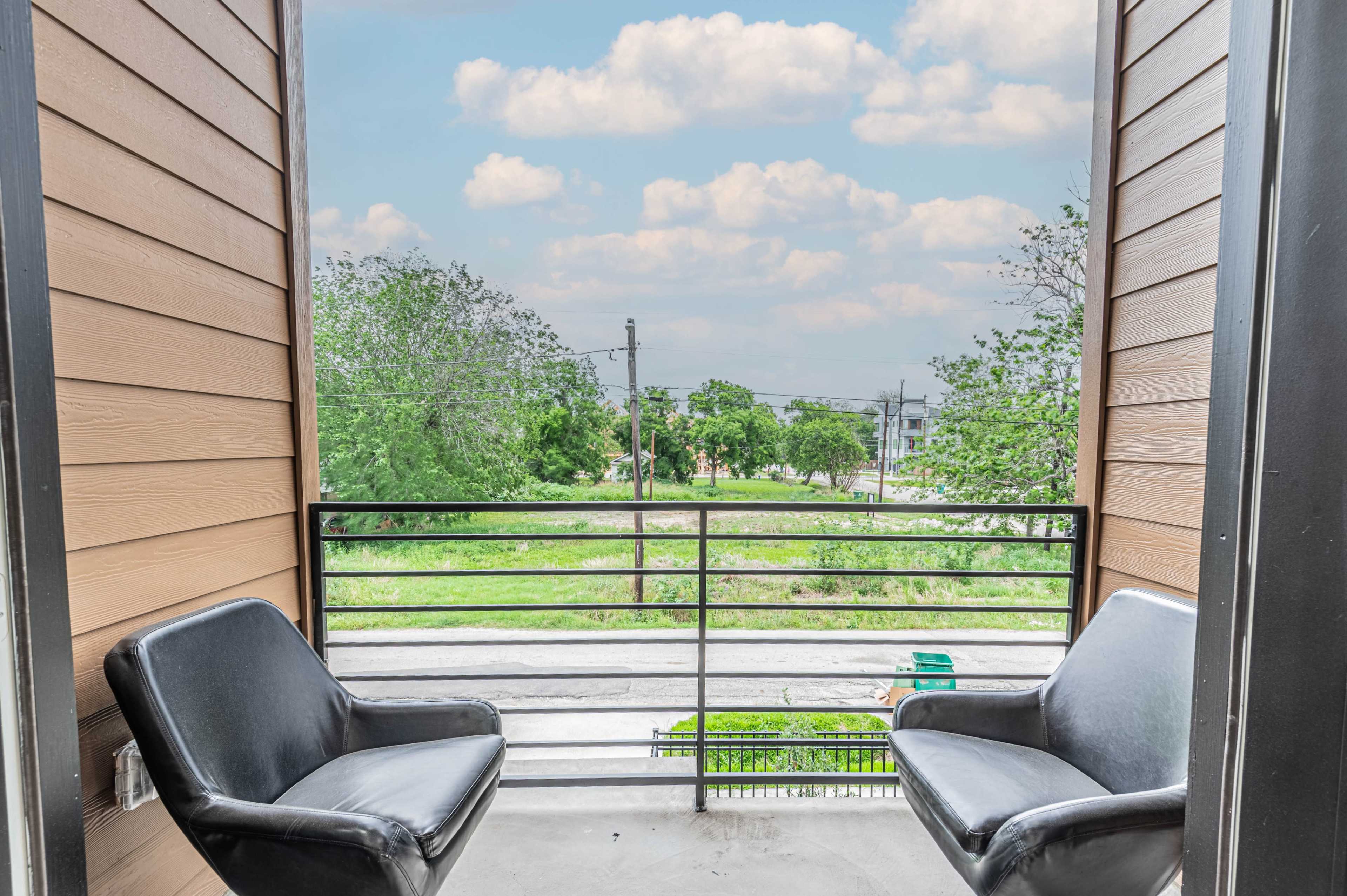 A balcony with two black chairs facing an open green area and a cloudy sky in the background.