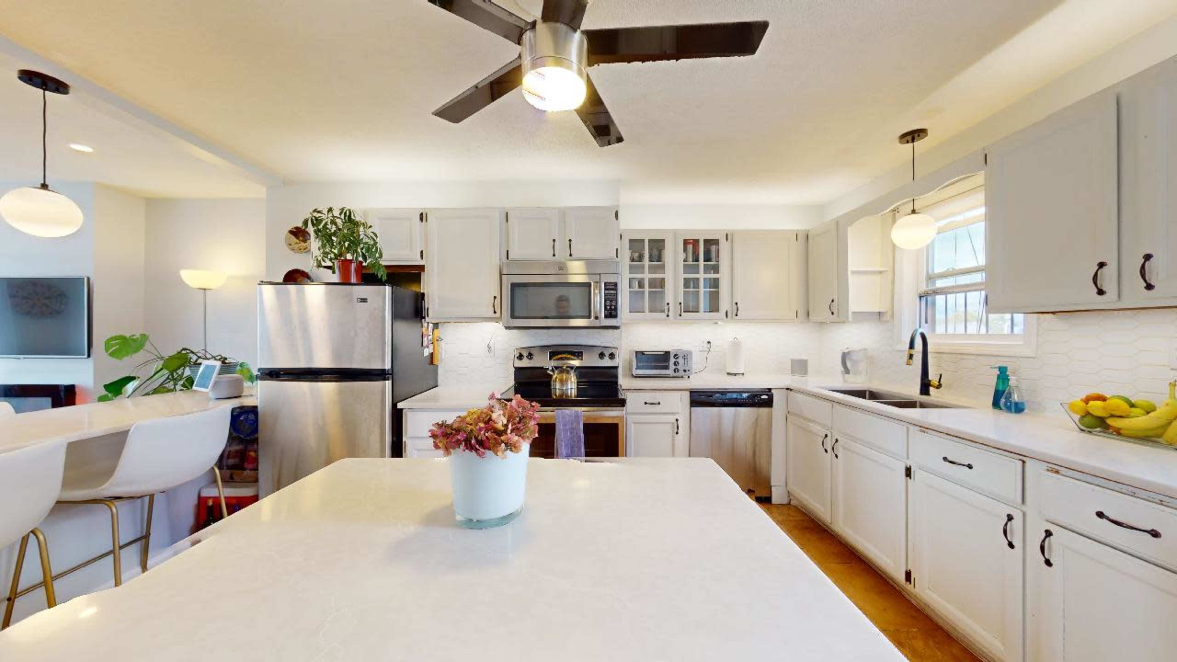 A modern kitchen features white cabinetry, stainless steel appliances, and a central island with a white countertop.
