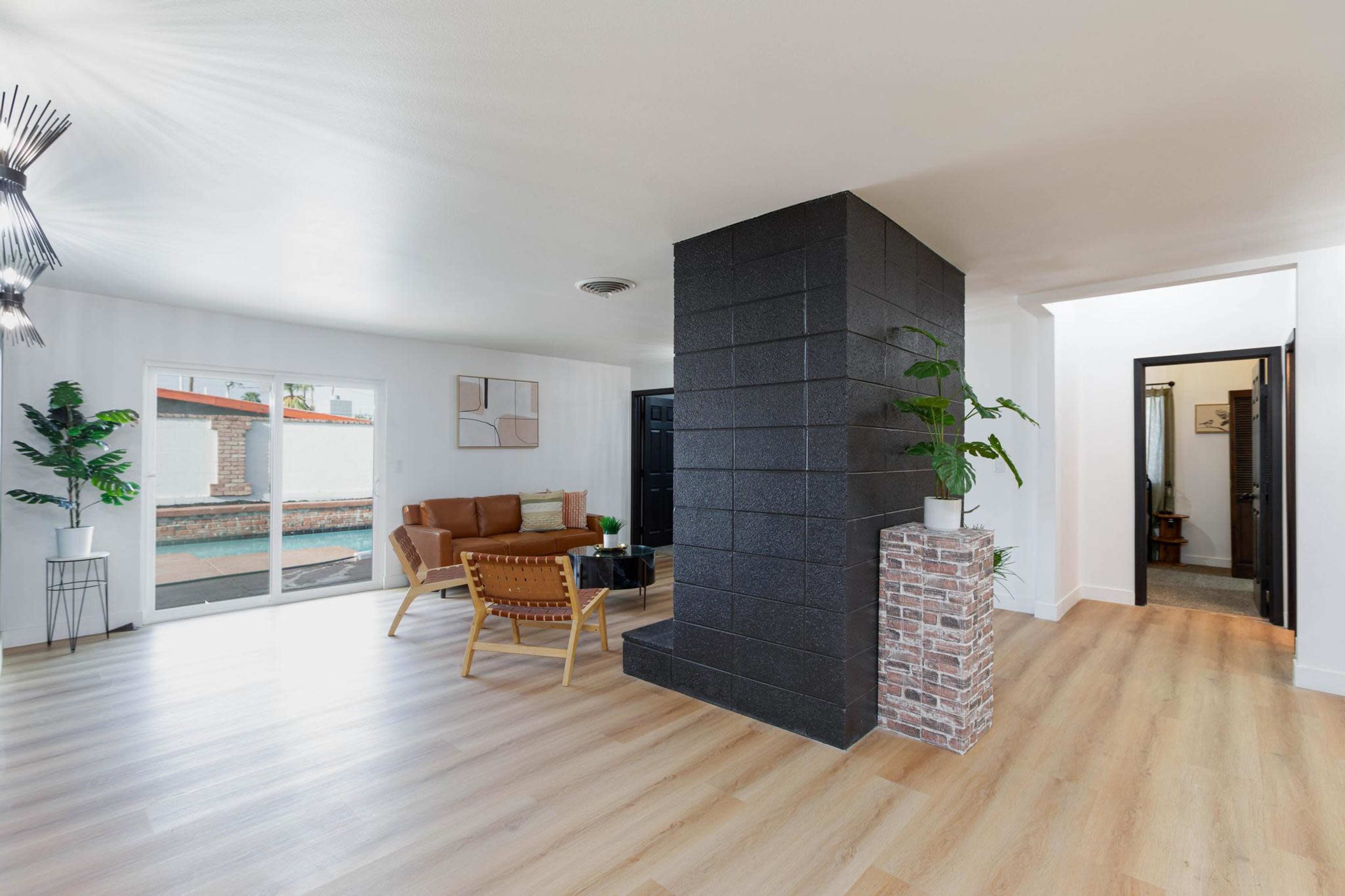 The image shows a modern living space with a black column, a sofa and chairs arranged around a coffee table, and large windows allowing natural light.