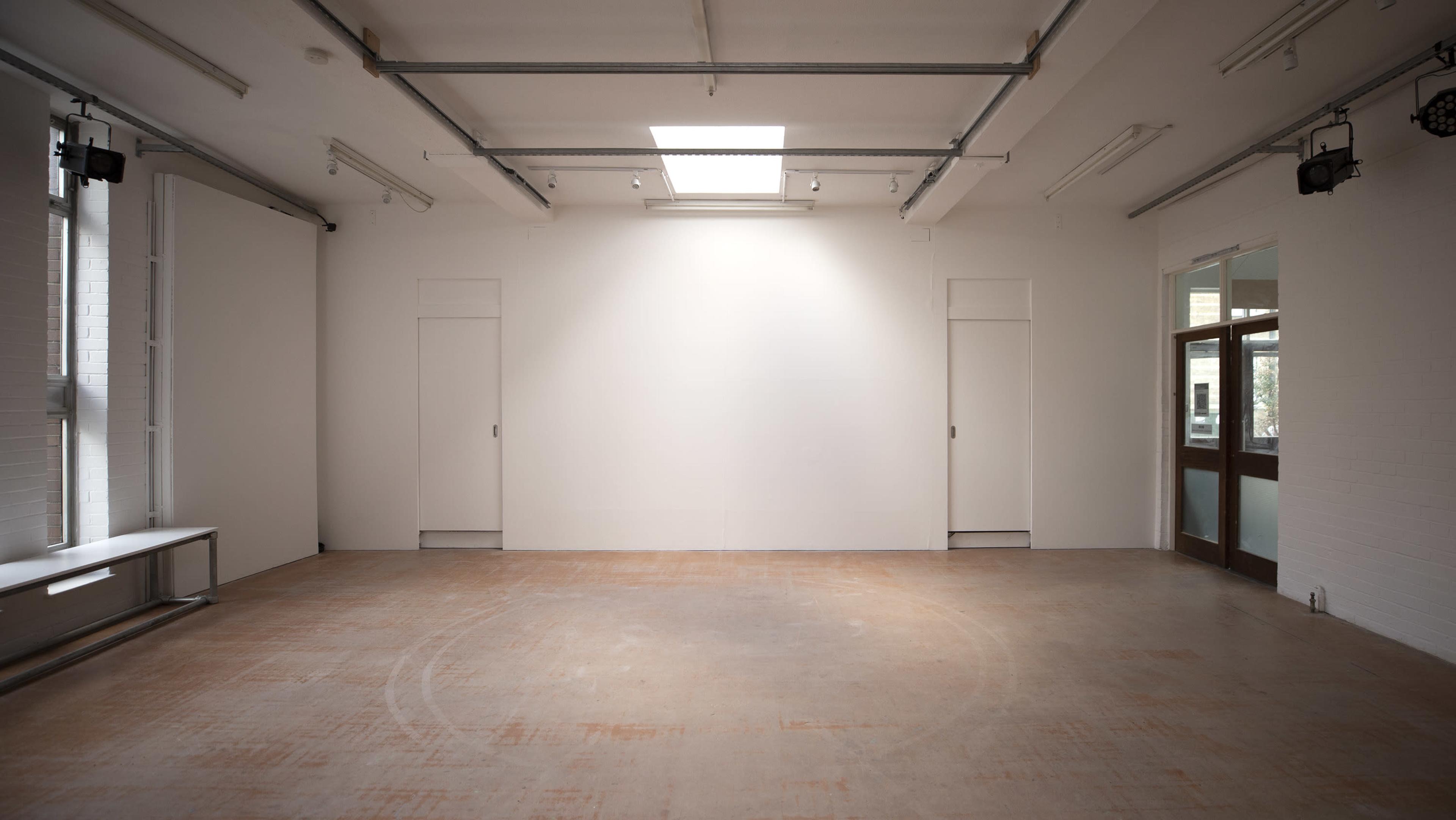A spacious, empty room with white walls, a concrete floor, and two closed doors on one side.