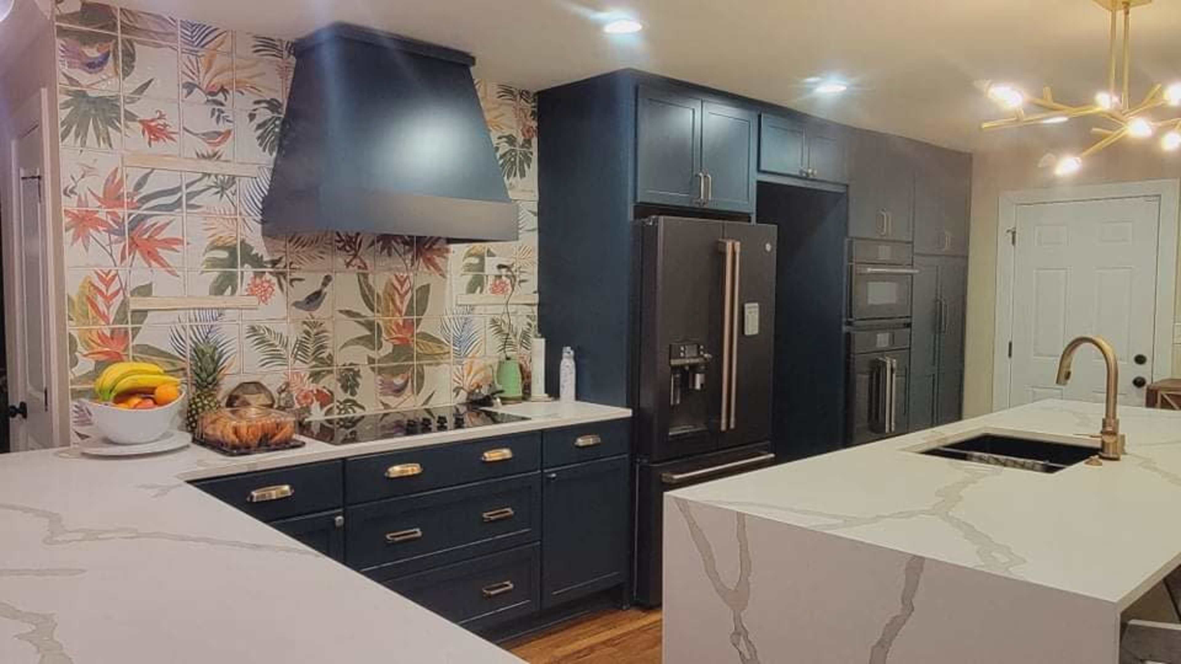A modern kitchen features dark cabinets, a floral wallpaper backsplash, and a large island with a sink and countertop appliances.