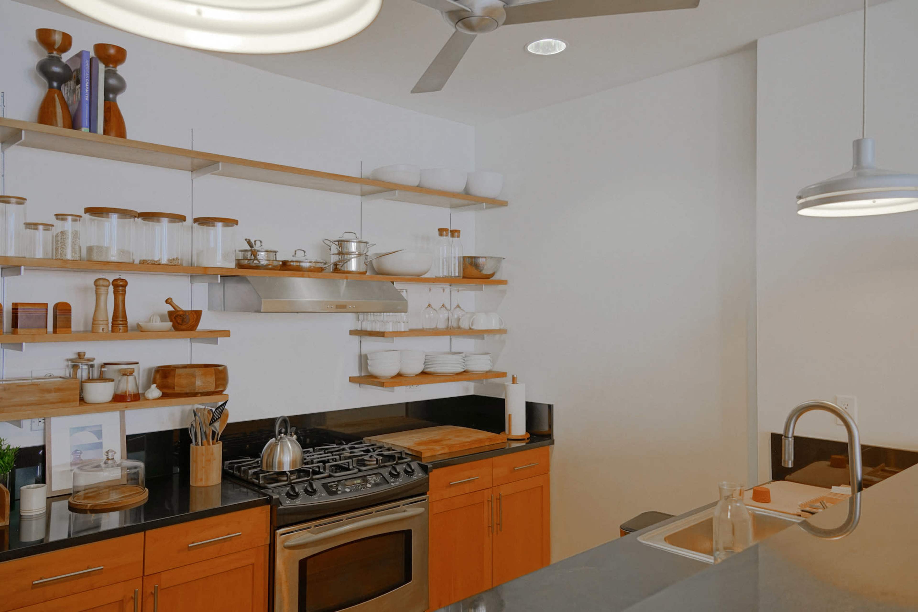 A modern kitchen with open shelves displaying glassware and kitchen tools, a stainless steel stove, and a sleek countertop.