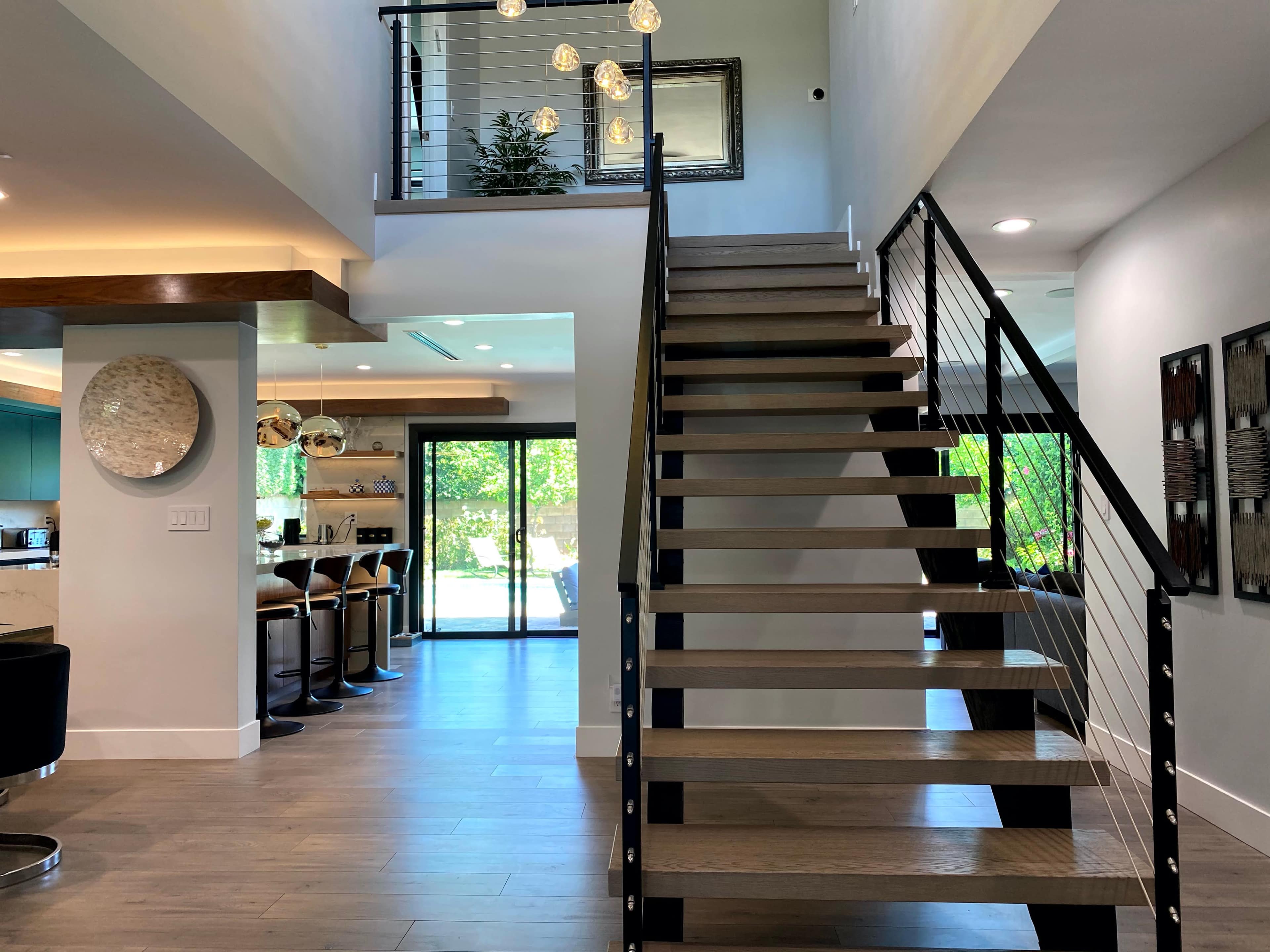 A modern interior with a staircase leading to an upper level, adjacent to a dining area and large windows that provide a view of the outdoors.