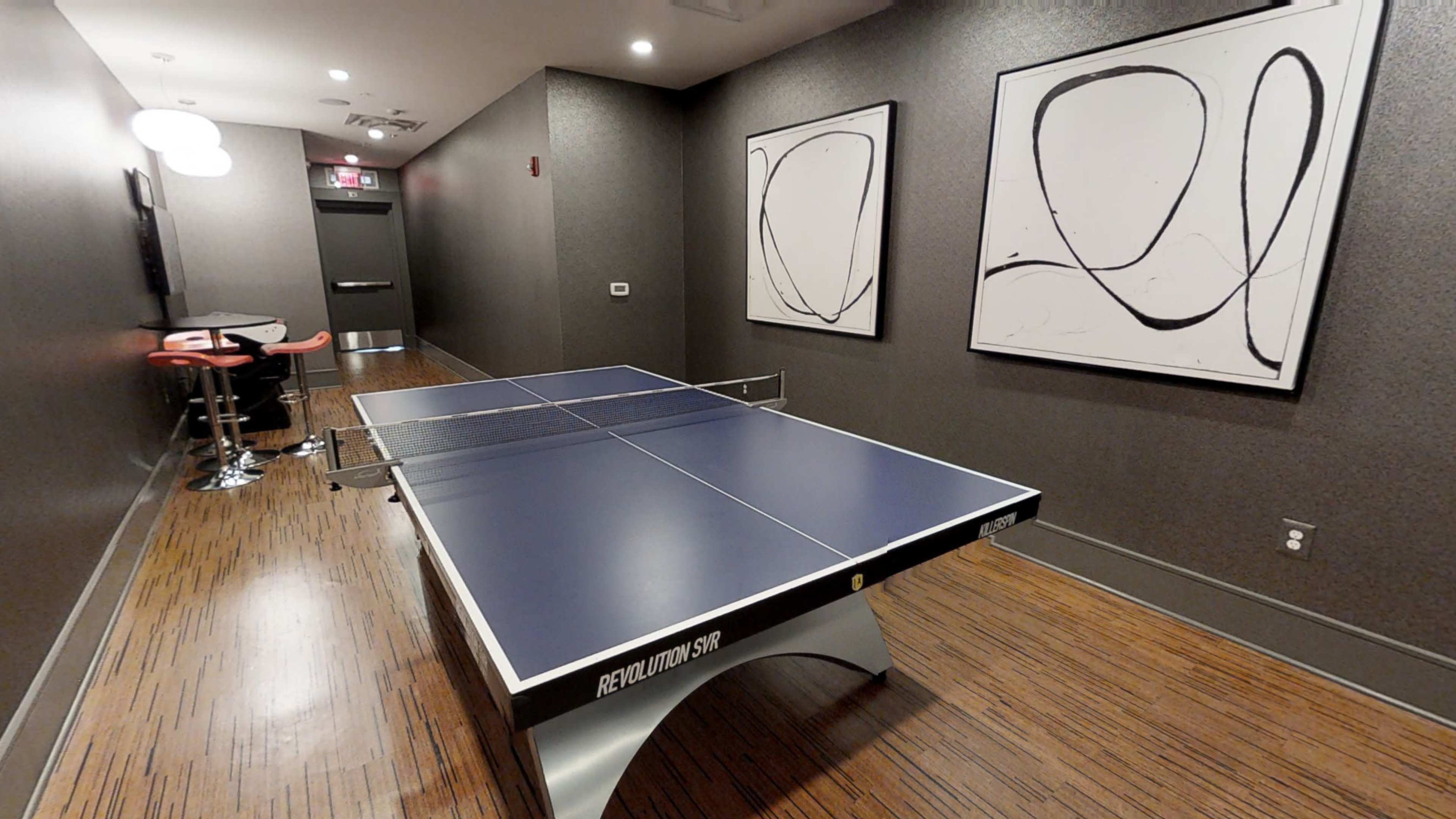A ping pong table located in a hallway with modern artwork on the walls and a small seating area nearby.