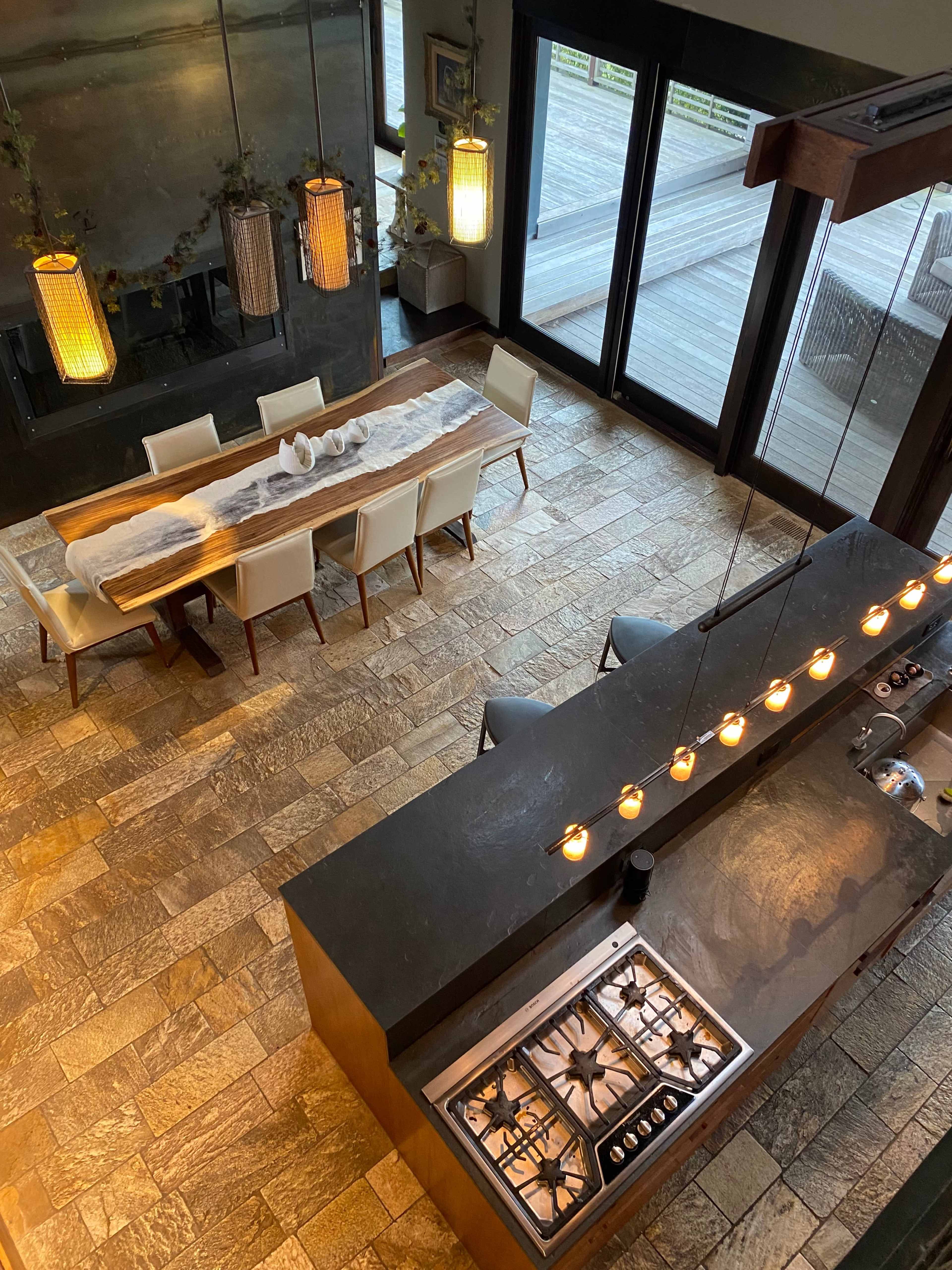 A spacious dining area with a long wooden table surrounded by chairs, adjacent to a kitchen island topped with dark stone and equipped with a stove.
