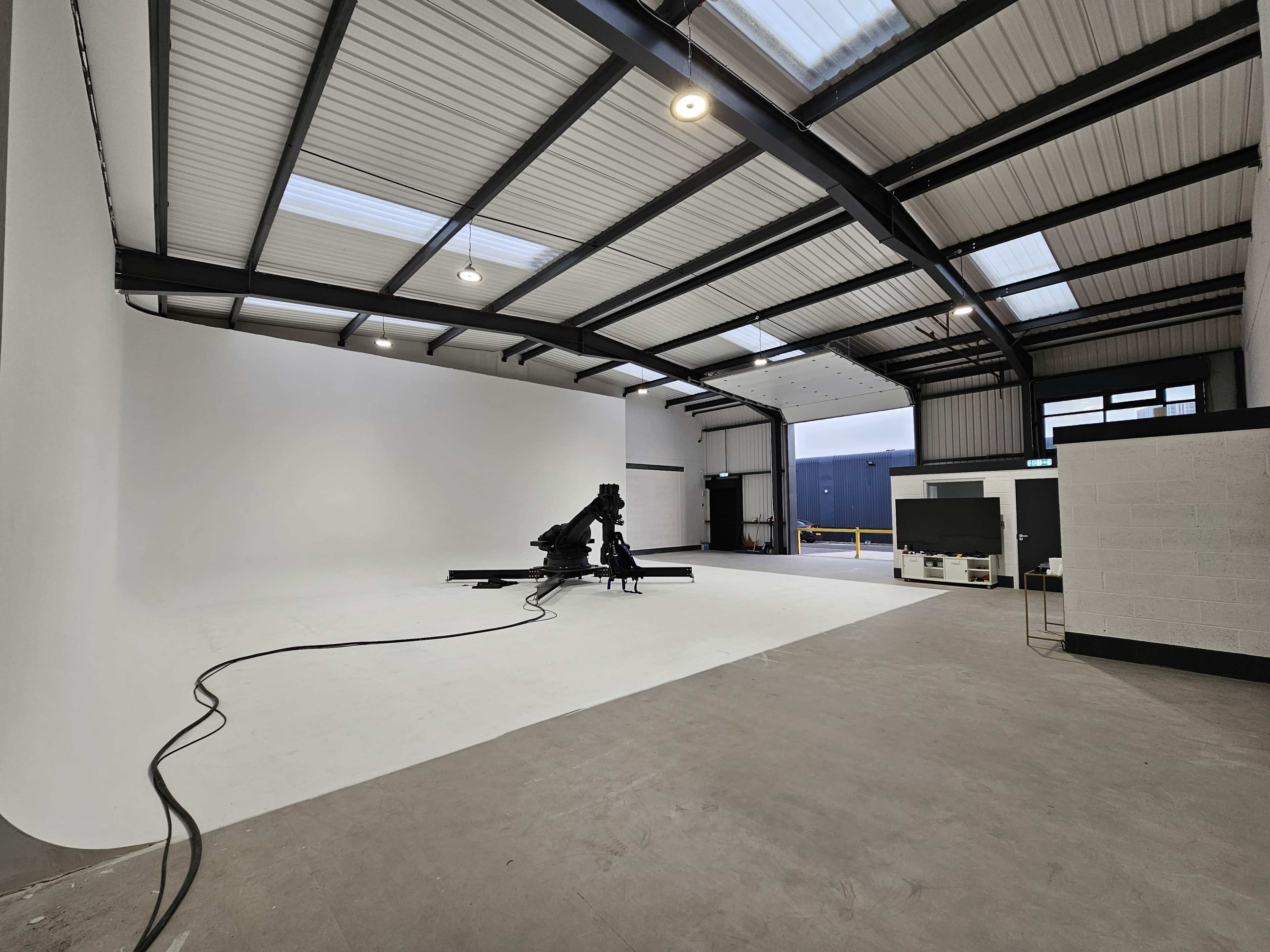 A spacious studio features a large white backdrop and a robotic arm positioned on a black platform.
