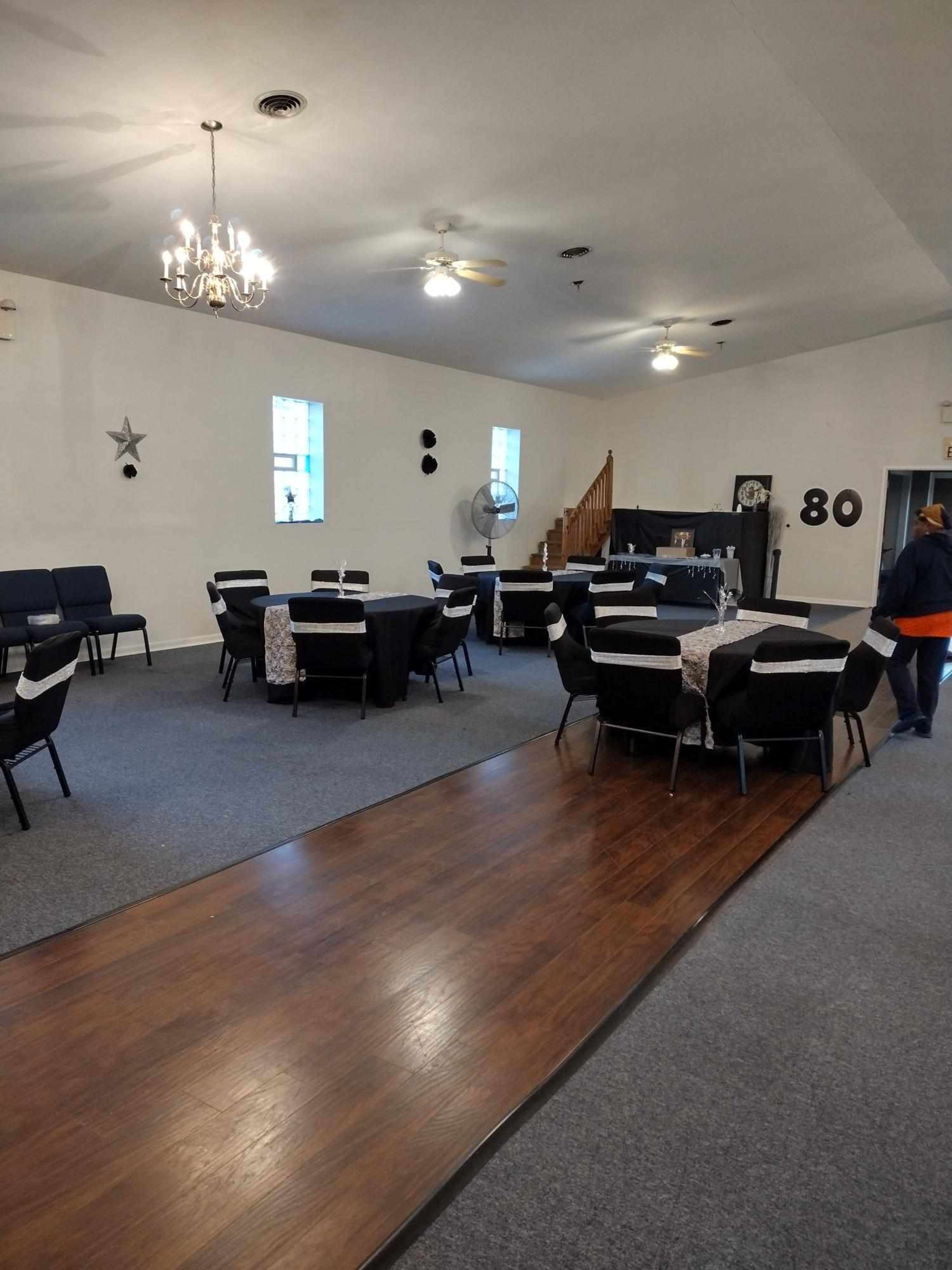 A spacious event room arranged with tables and chairs, featuring a wooden floor section and decorative elements like a chandelier and wall decor.