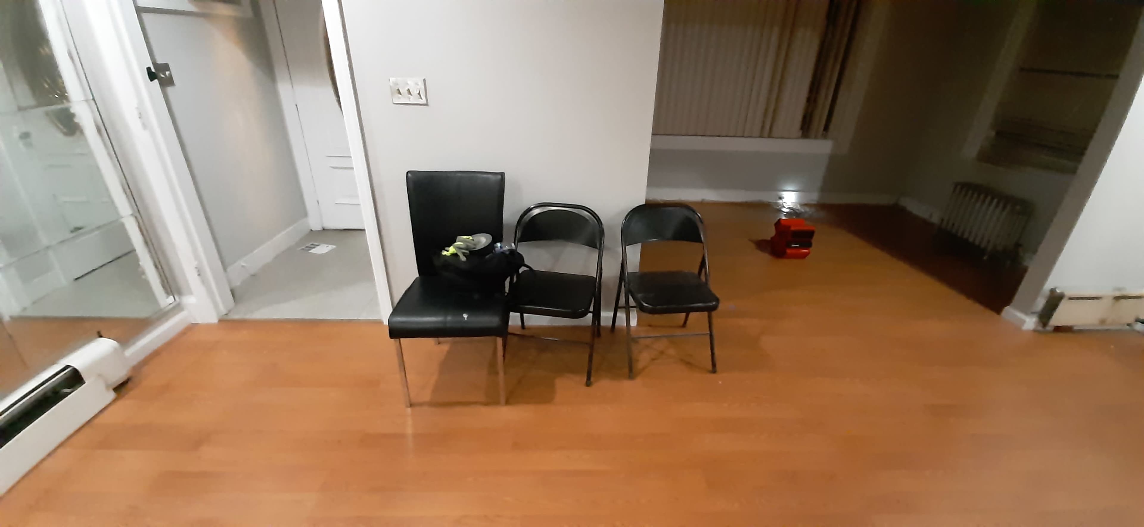 Three chairs, two black metal chairs and one black leather chair, positioned on a wooden floor in a sparsely furnished room.