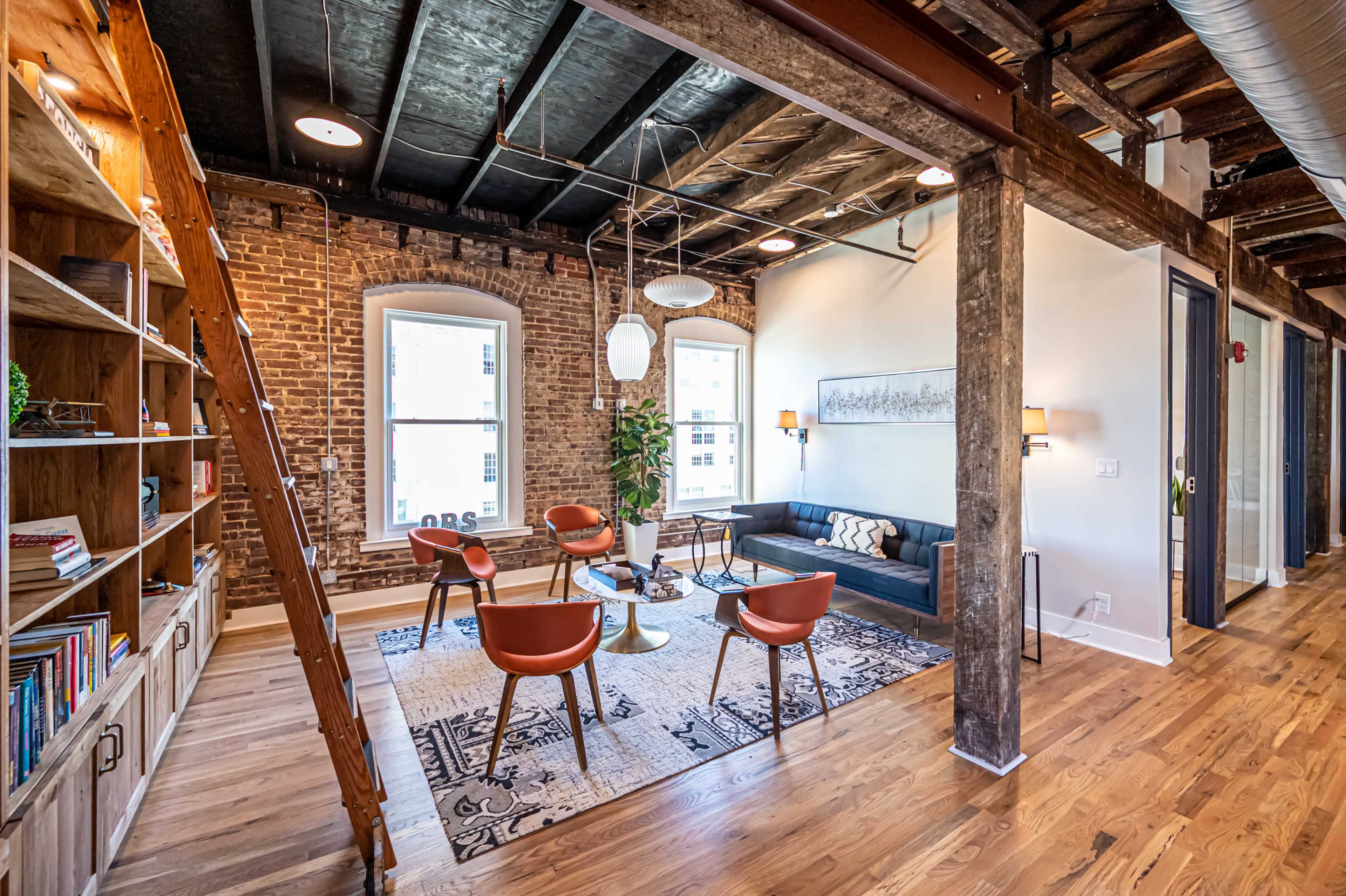 A modern living room featuring exposed brick walls, wooden beams, and stylish furniture arranged around a central coffee table.