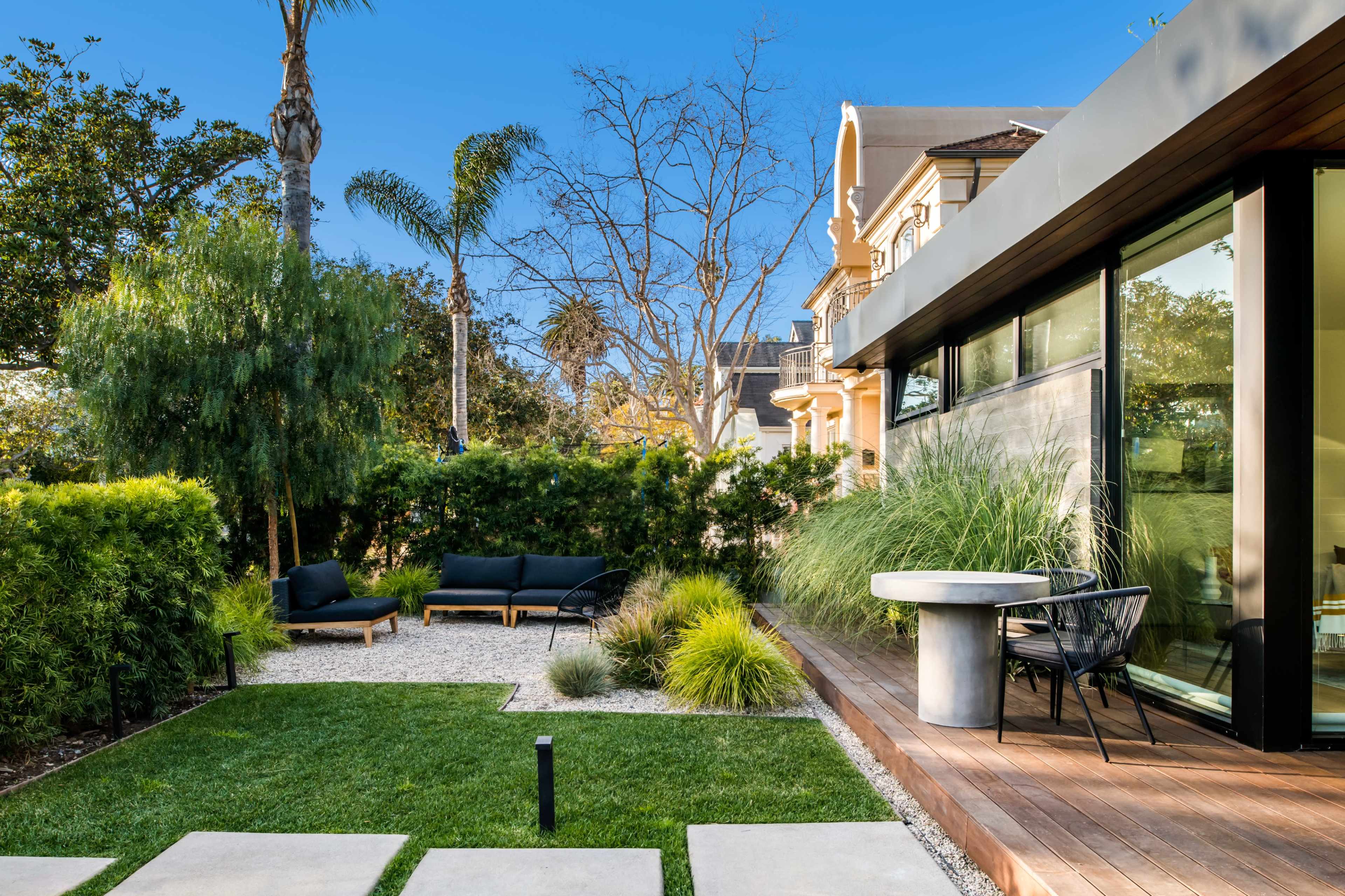 A modern backyard with a patio area, lounge seating, landscaped grass, and surrounding greenery.