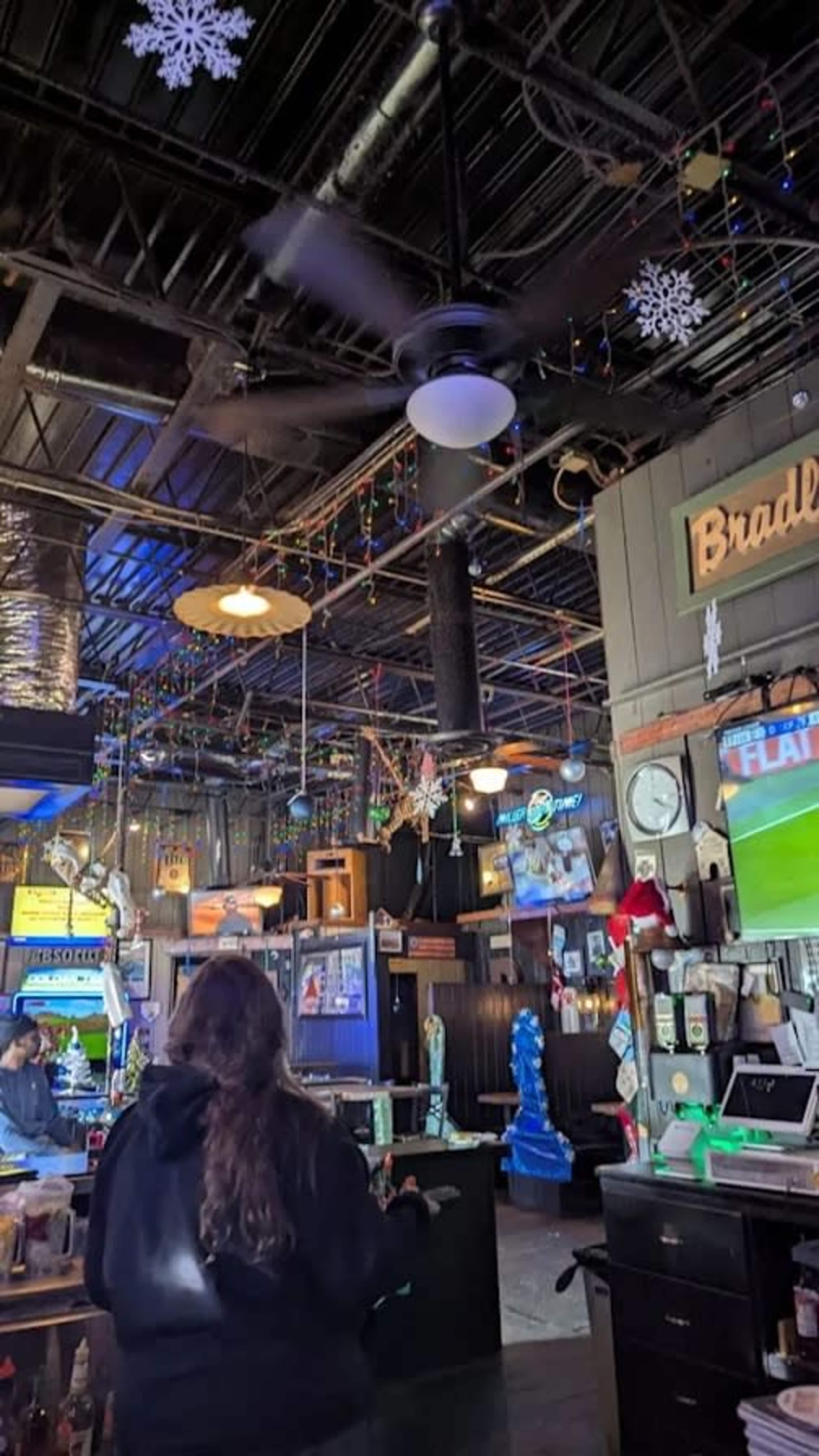 The interior of a bar features a tall ceiling with a fan, colorful lights, and various decorations, including snowflakes.