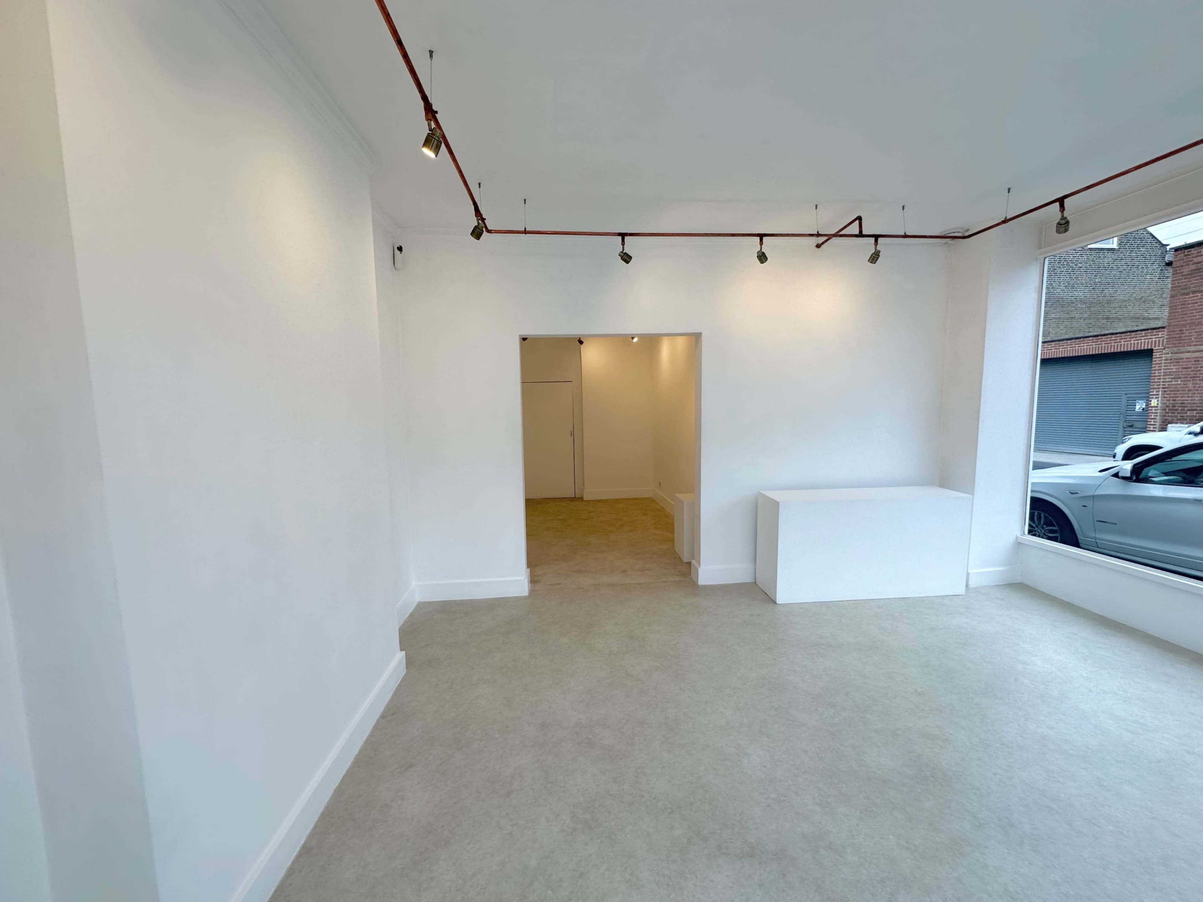 The image shows a minimalist room with white walls, a light-colored floor, and a doorway leading to a separate area.