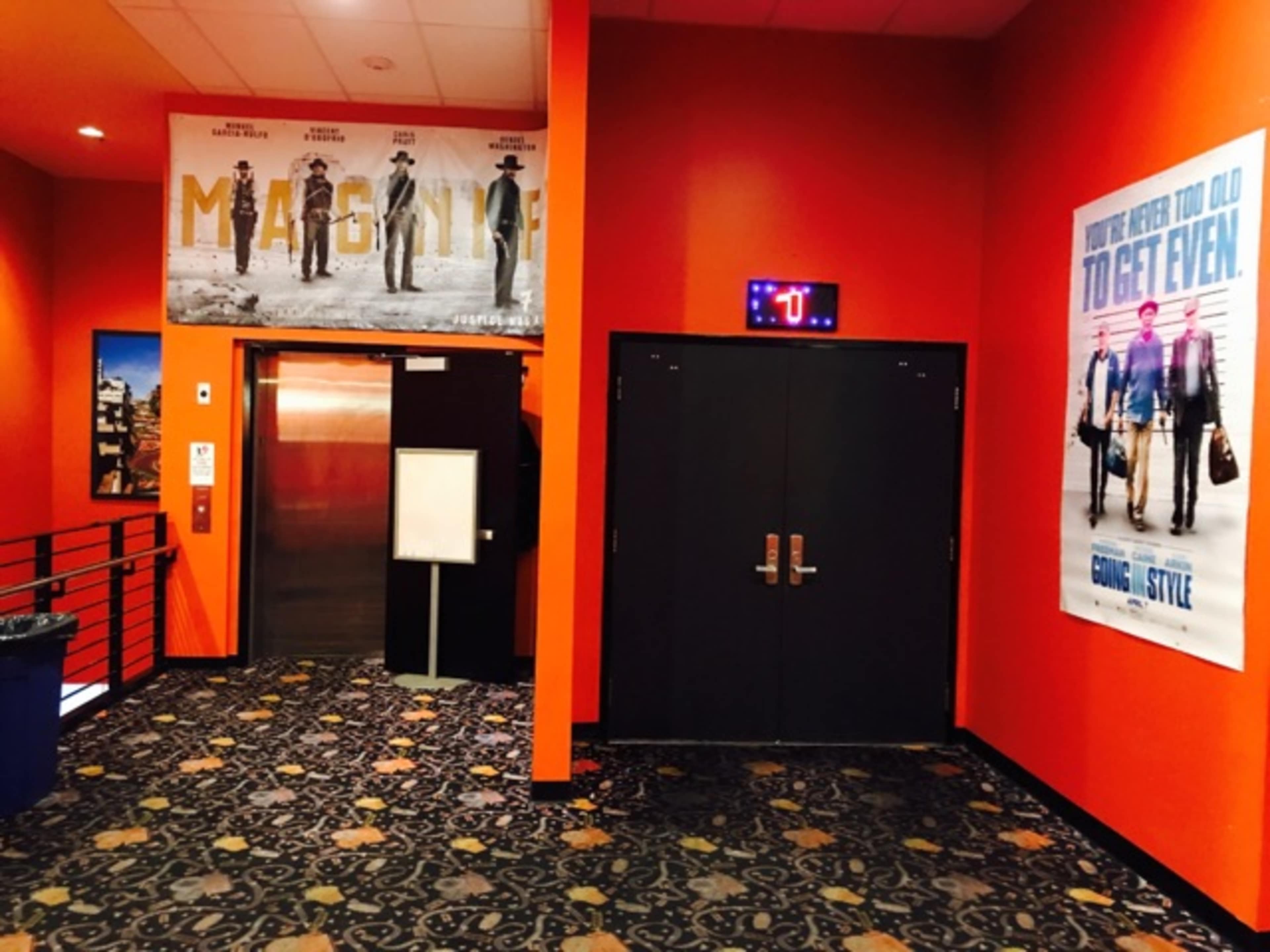 A brightly colored theater hallway with movie posters on the walls and an elevator door on the left side.