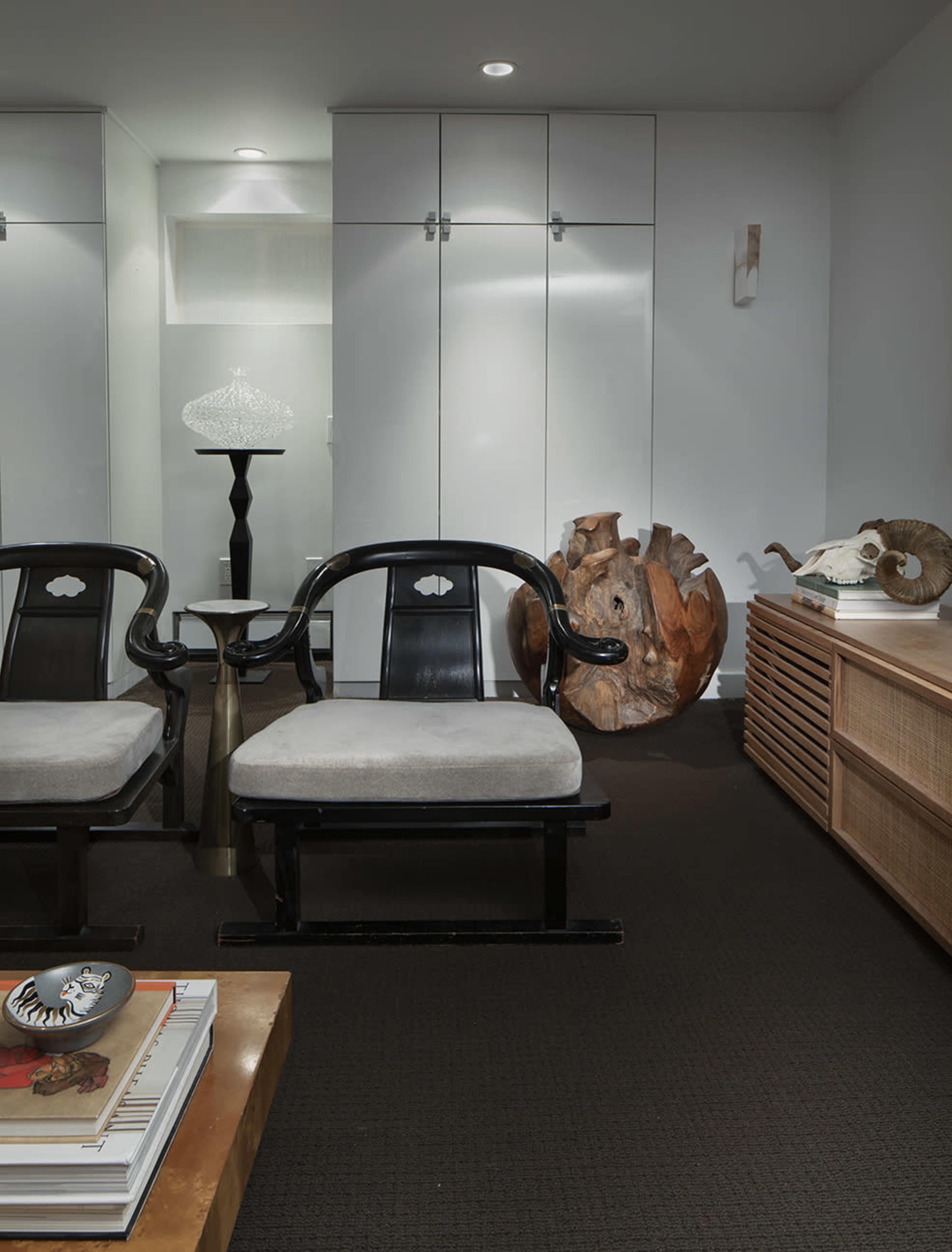 The image shows a modern interior space with two black wooden chairs, a small side table, decorative objects, and a light-colored cabinet in the background.